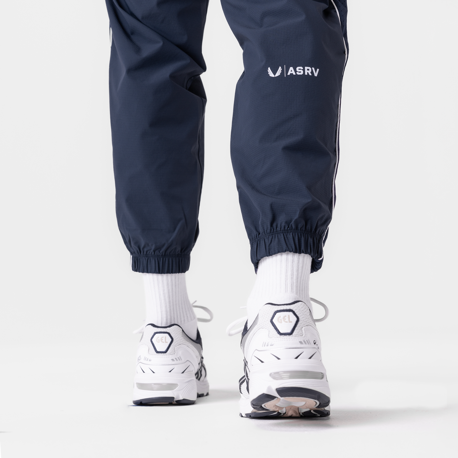 Navy ripstop track pants worn with white socks and sneakers, shown from waist down