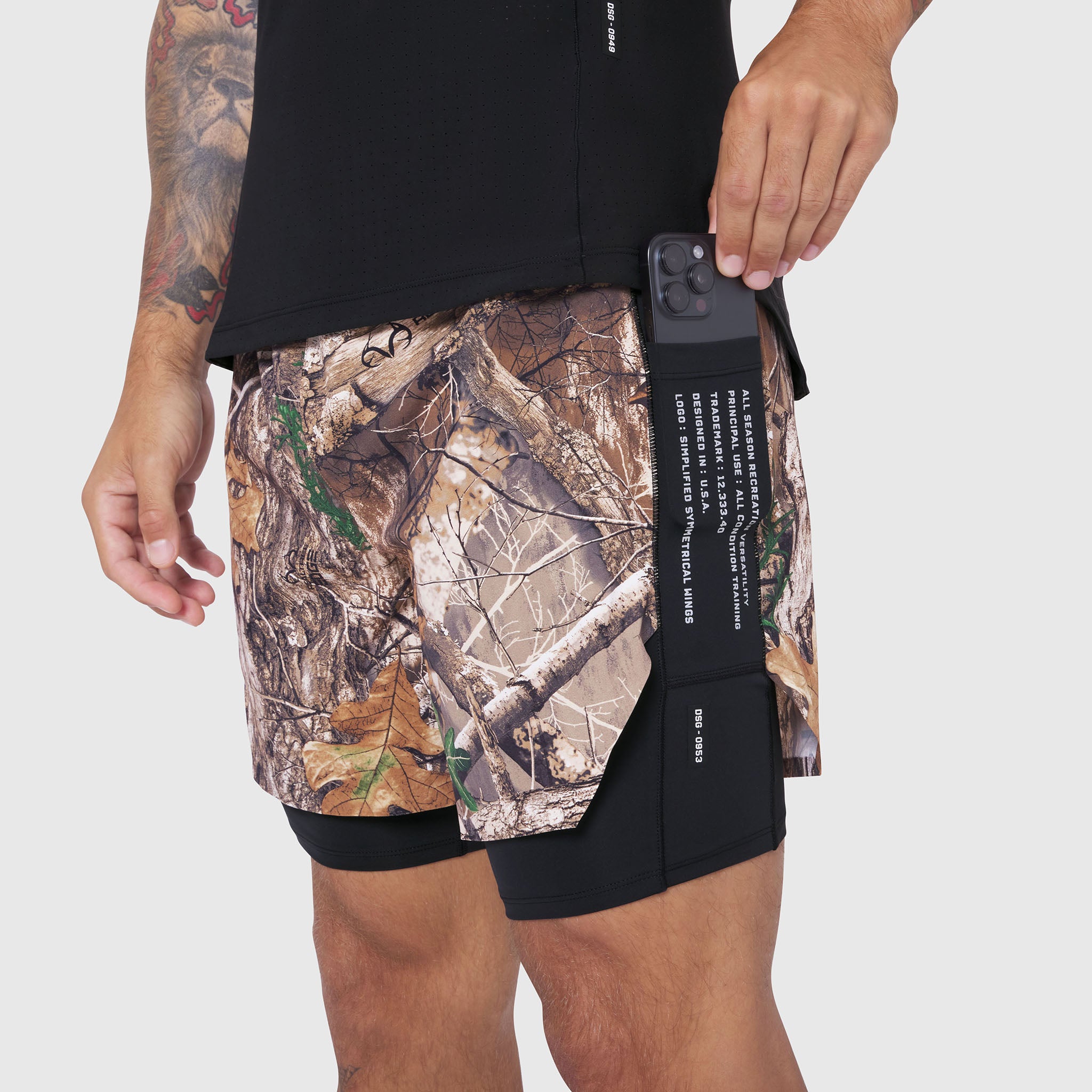 Aerotex Hybrid Liner Short in Realtree Edge camo with black side panel, worn by model holding phone