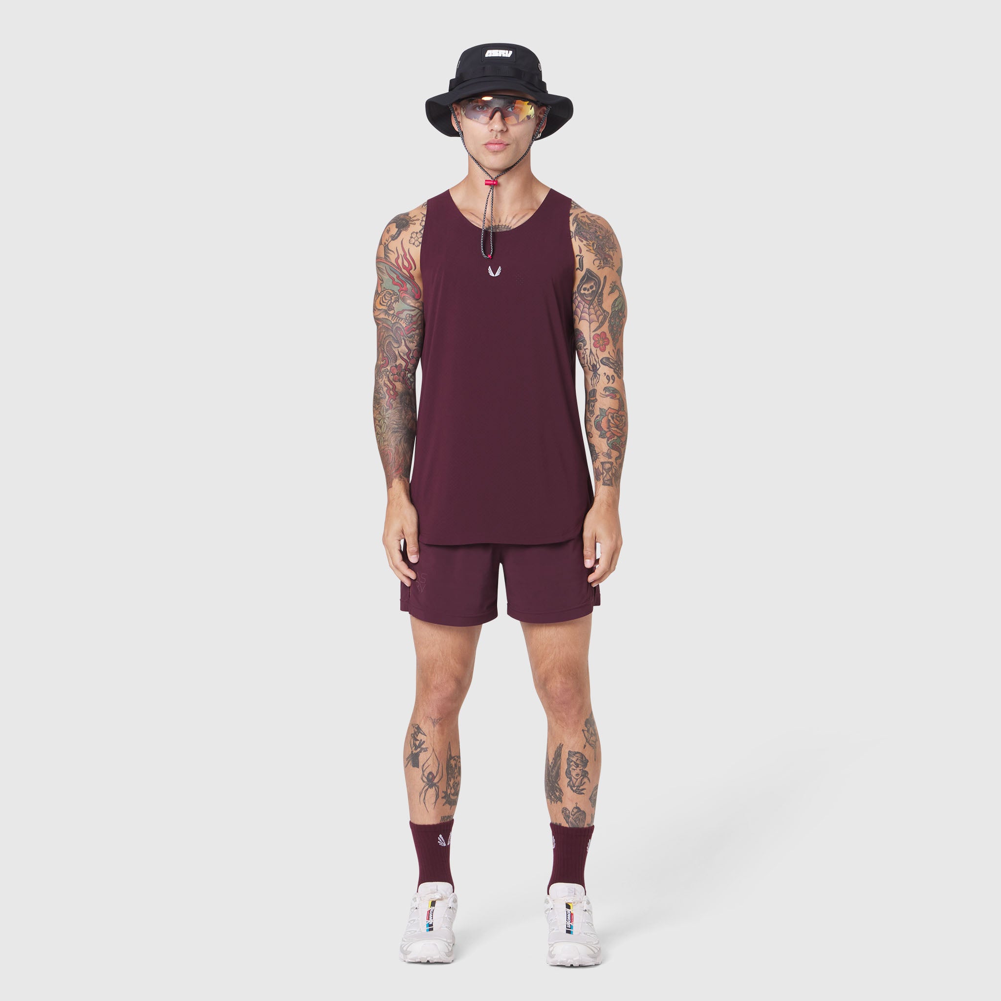 Aerotex Perforated Run Tank in merlot with matching shorts, modeled with white sneakers and black bucket hat