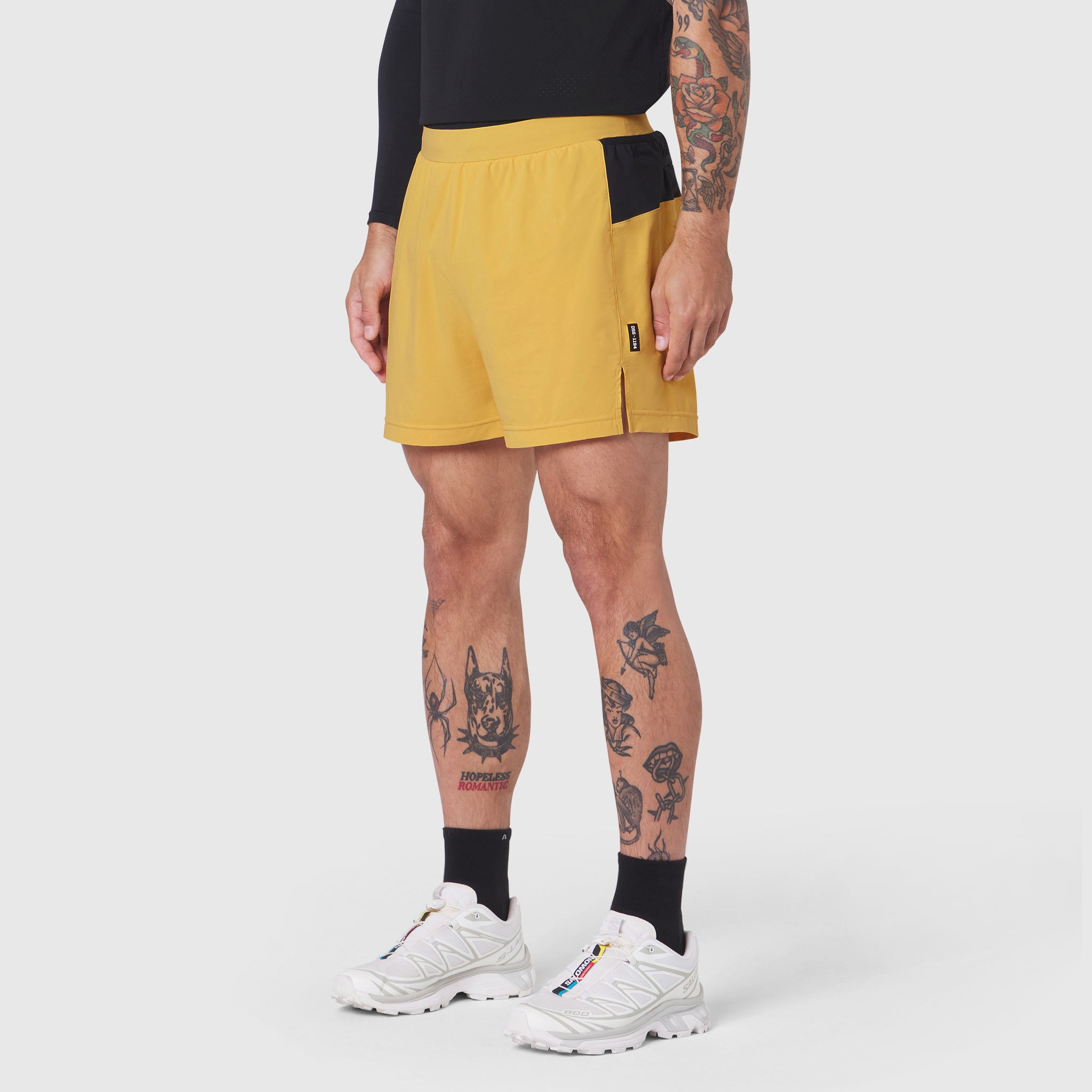 Aerotex Distance Run Short in amber yellow with black side panels, worn by model with white sneakers