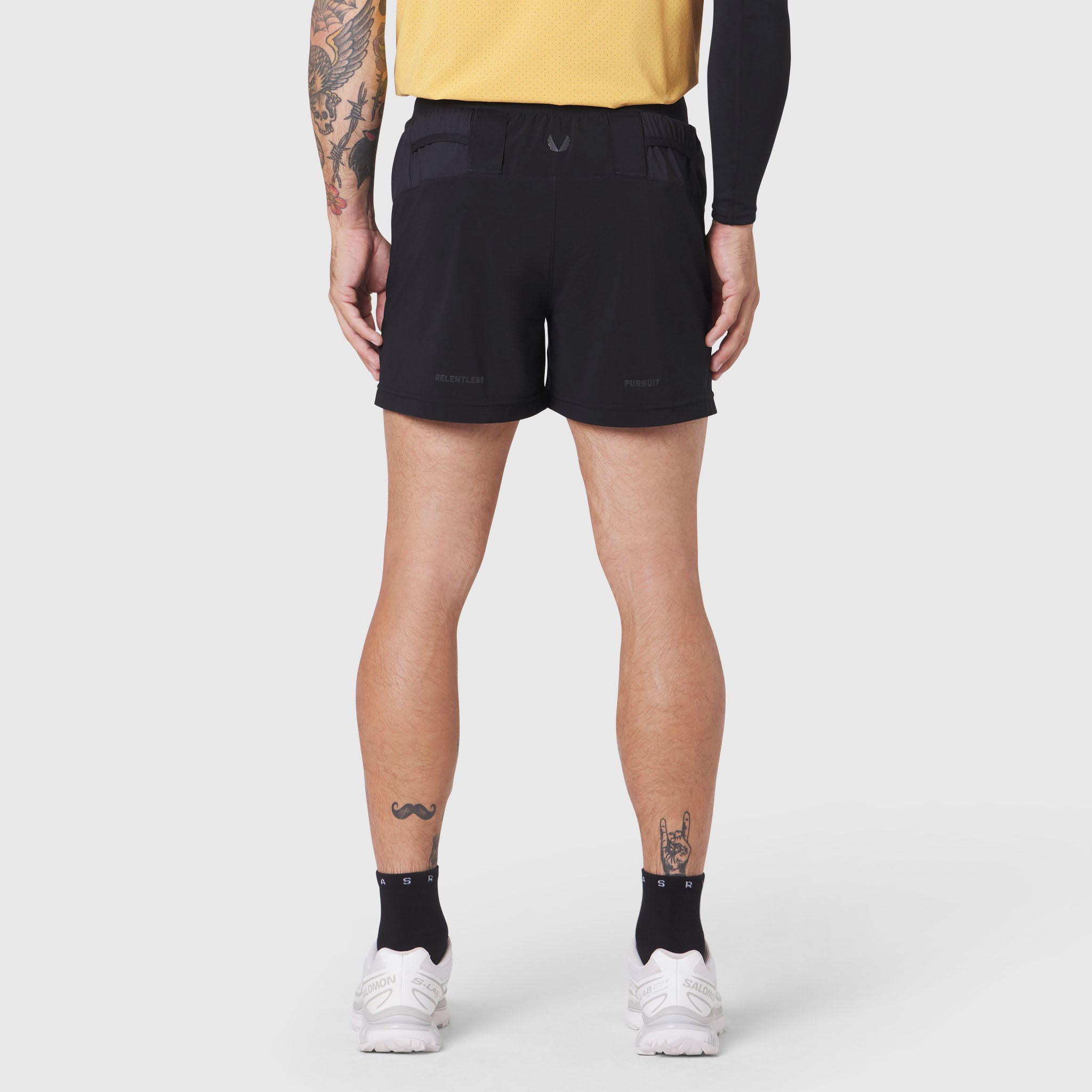 Aerotex Distance Run Short in black, rear view on model wearing yellow top and white sneakers