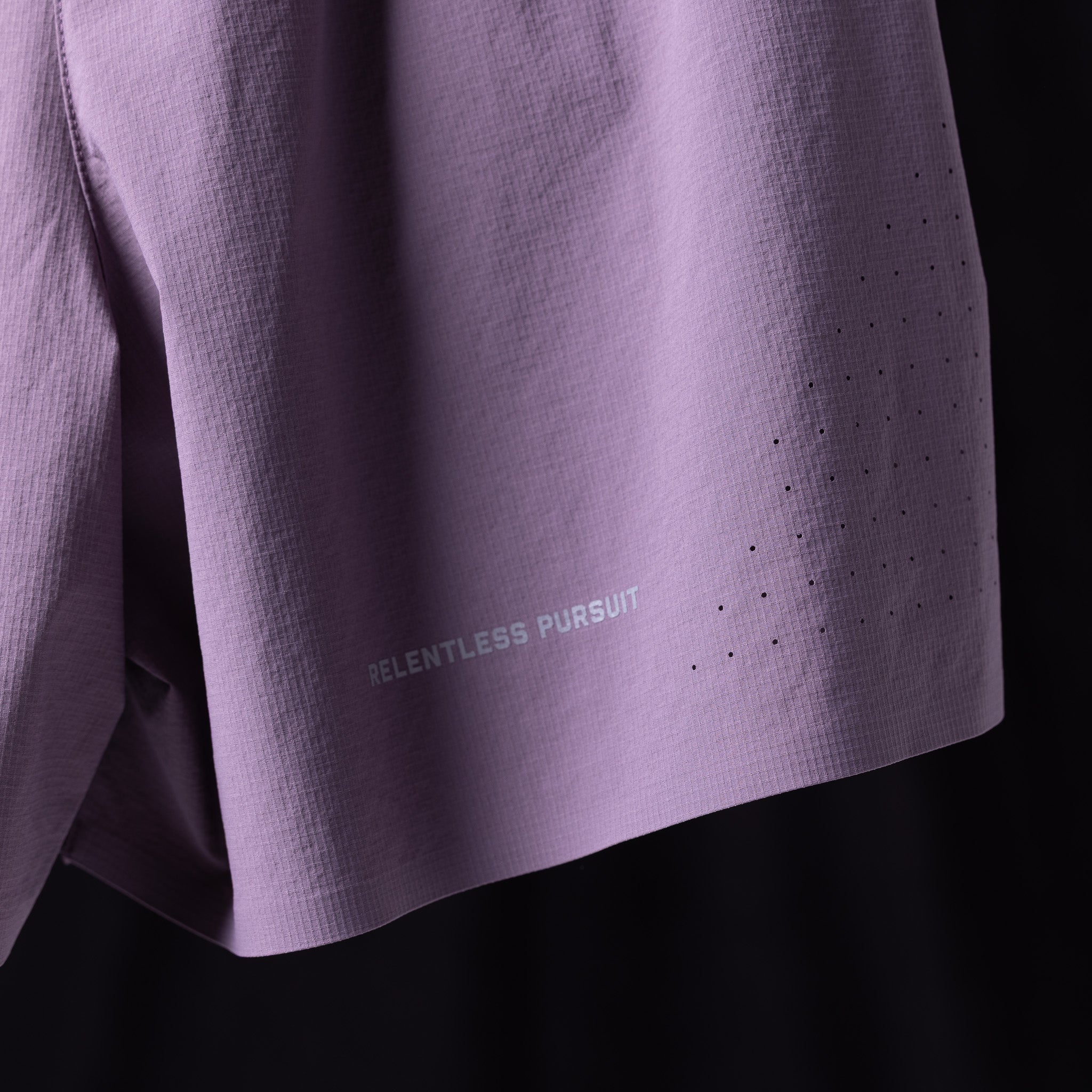 WN'23 6" Perforated Short in lavender, detail shot of fabric and 'Relentless Pursuit' branding
