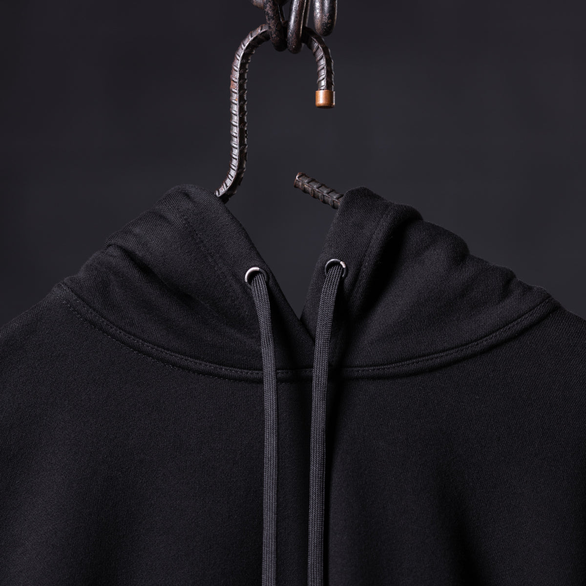 FA'20 Contrast Thread Hoodie in black, hung on metal hook showing drawstring detail