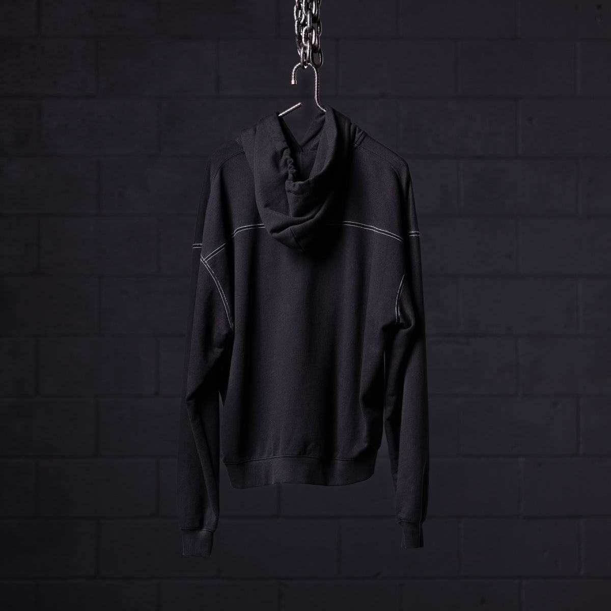Black contrast thread hoodie displayed on hanger against dark brick wall background