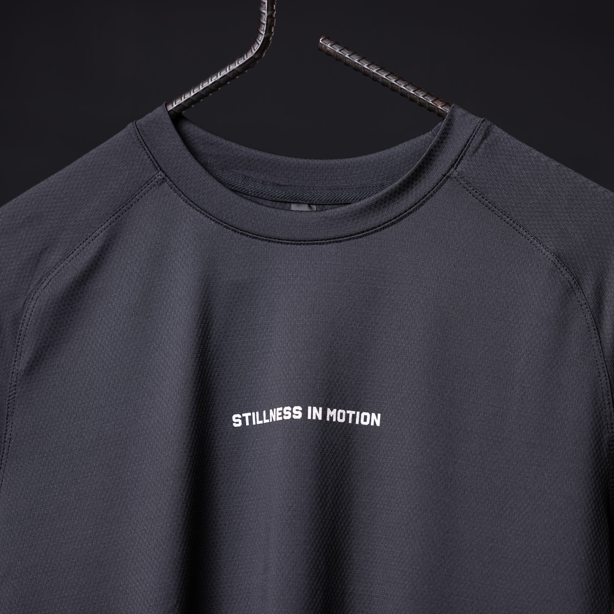 SM'22 Established Tee in charcoal gray on hanger, front view showing 'Stillness in Motion' text