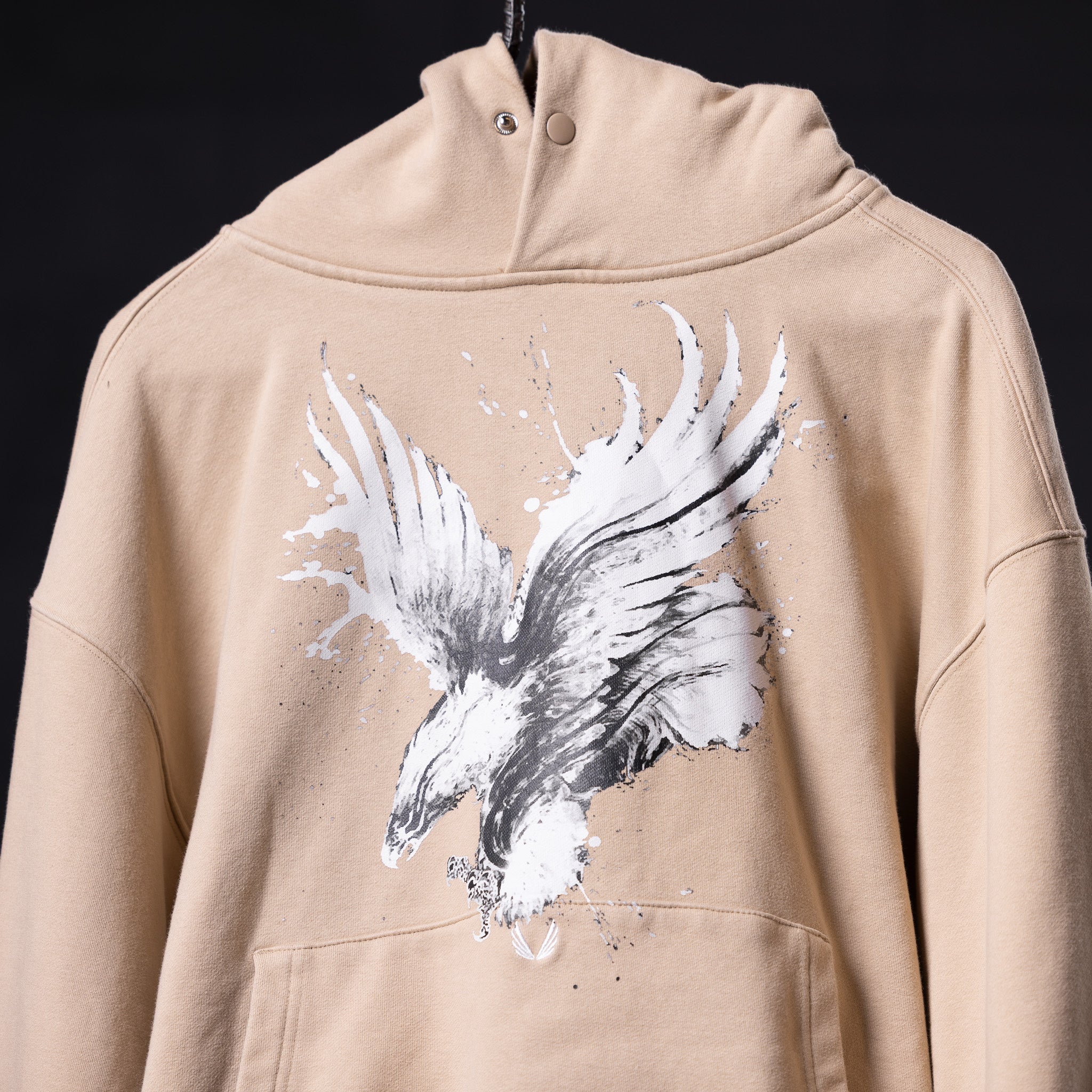 Beige graphic hoodie with white and gray feather wing design, displayed on model