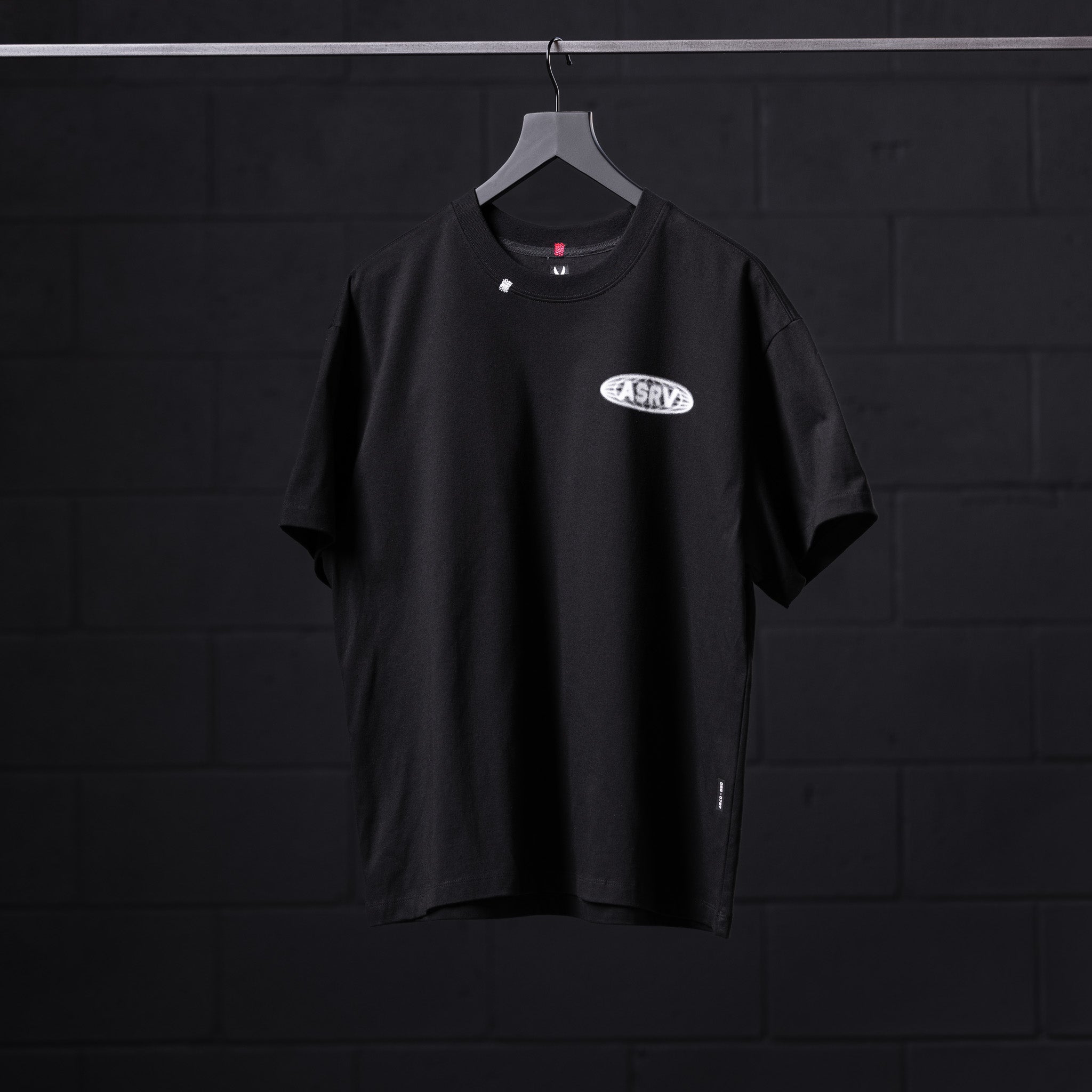 Black Tech Essential Relaxed Tee with Global Reach logo on hanger against dark background