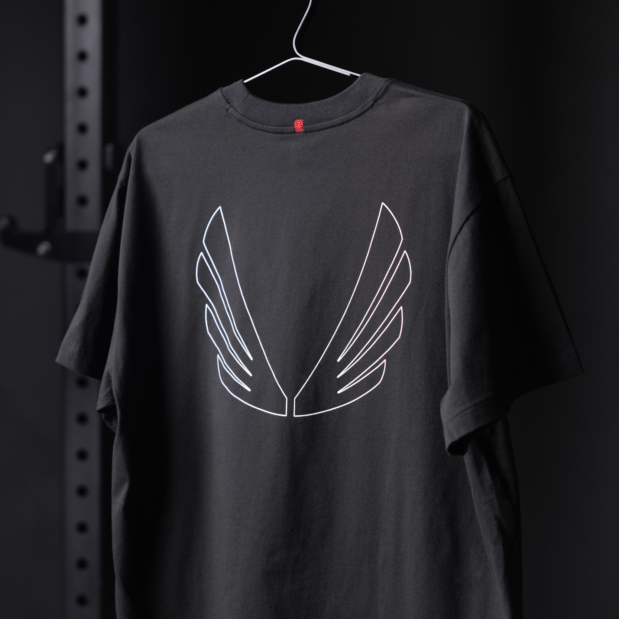Black Tech Essential Relaxed Tee with white wing outline design on hanger