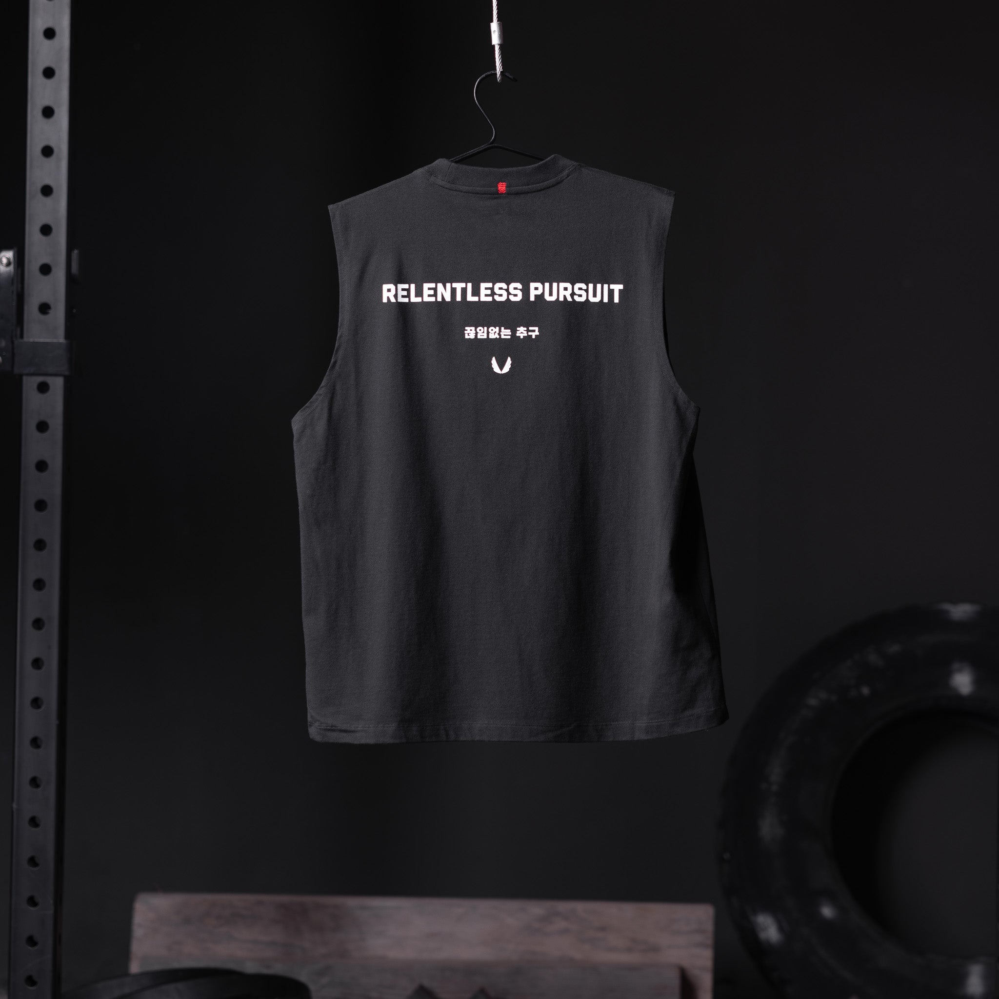 Black Tech Essential Relaxed Cutoff vest with 'Relentless Pursuit' text, hanging on hanger, back view