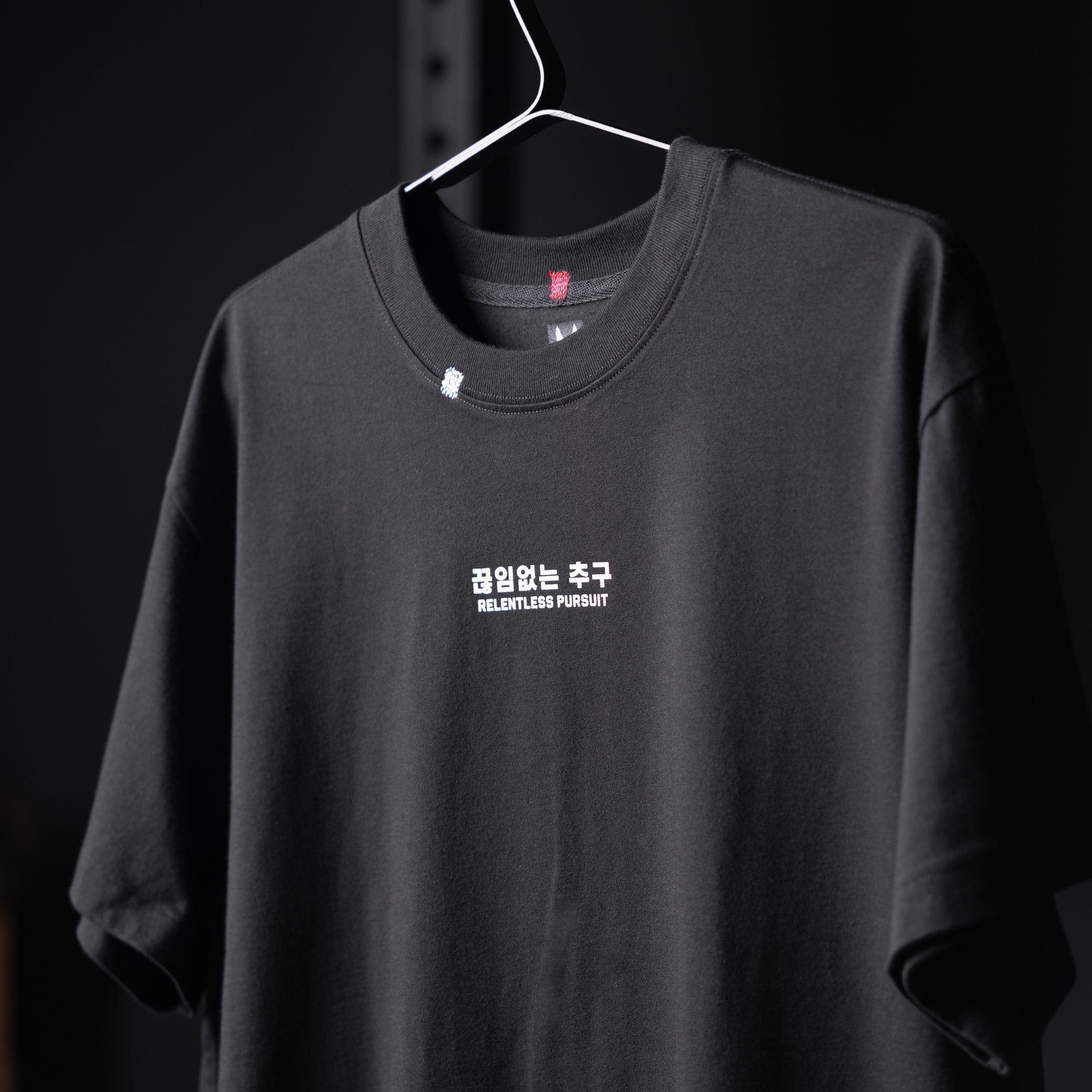 Black Tech Essential Relaxed Tee with 'Relentless Pursuit' graphic, displayed on hanger