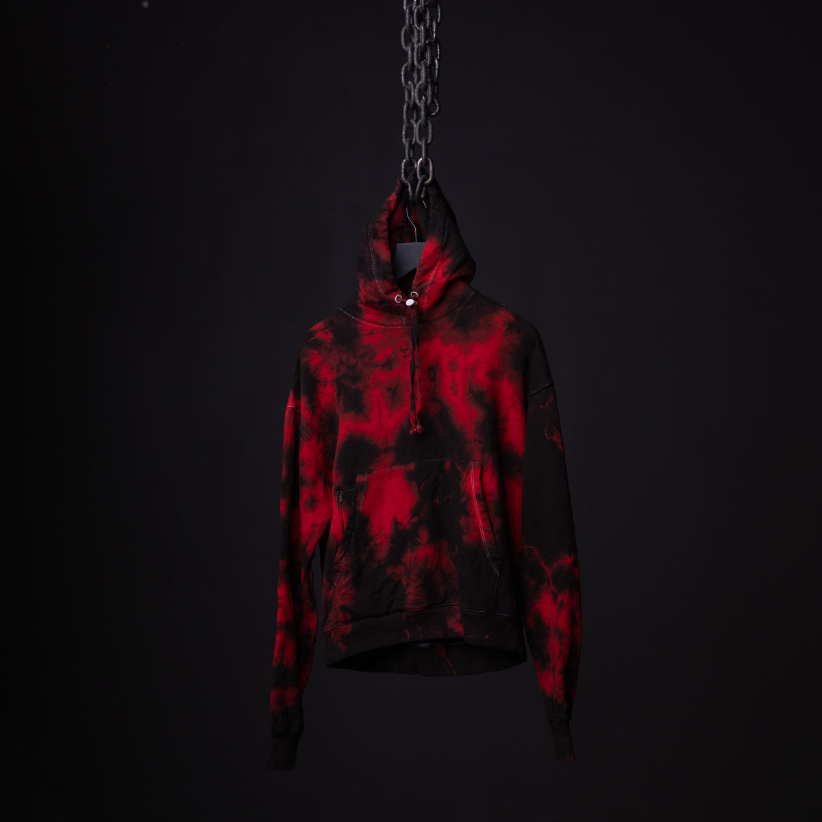 SM'22 Tie Dye Hoodie in red and black tie dye, suspended by chain against dark background