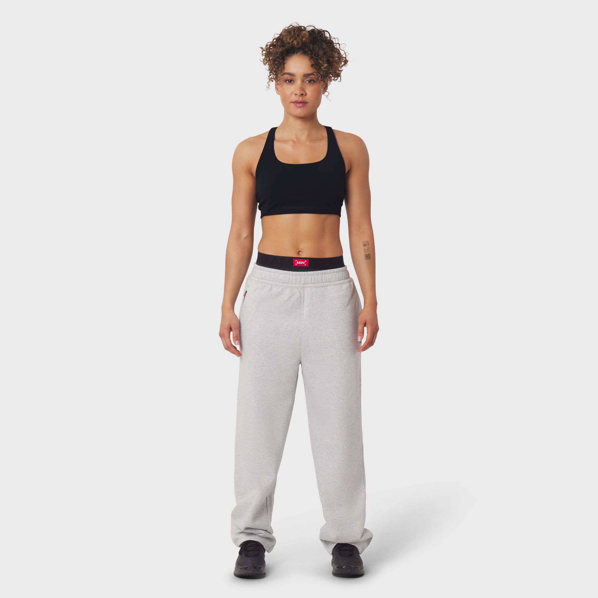 Model wearing black sports bra and grey joggers with black waistband detail, front view