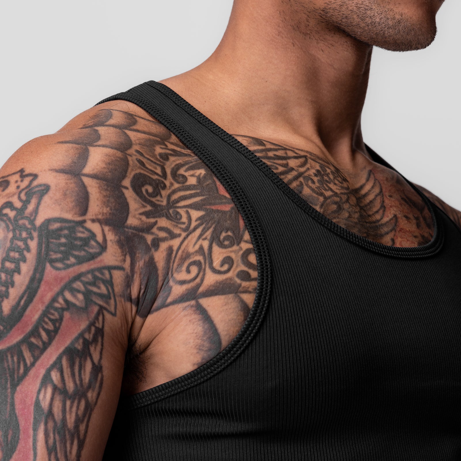Black Creora® Tech Ribbed Tank worn by model, showcasing shoulder tattoos, side view