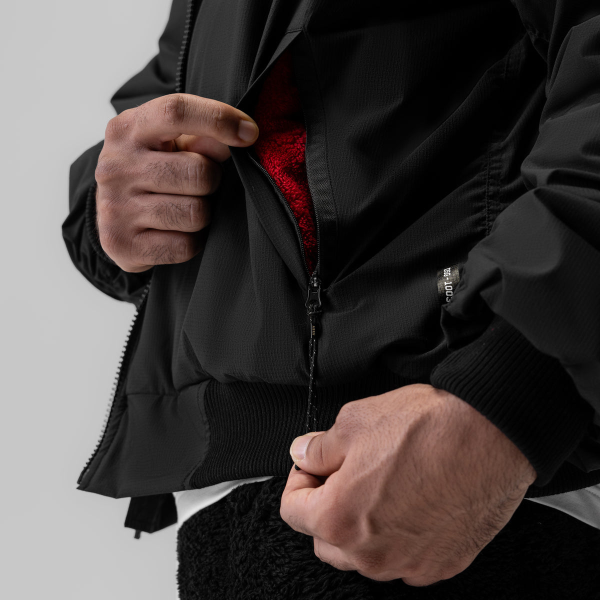 Sherpa-lined insulated bomber jacket in black, worn and zipped open to show red interior lining