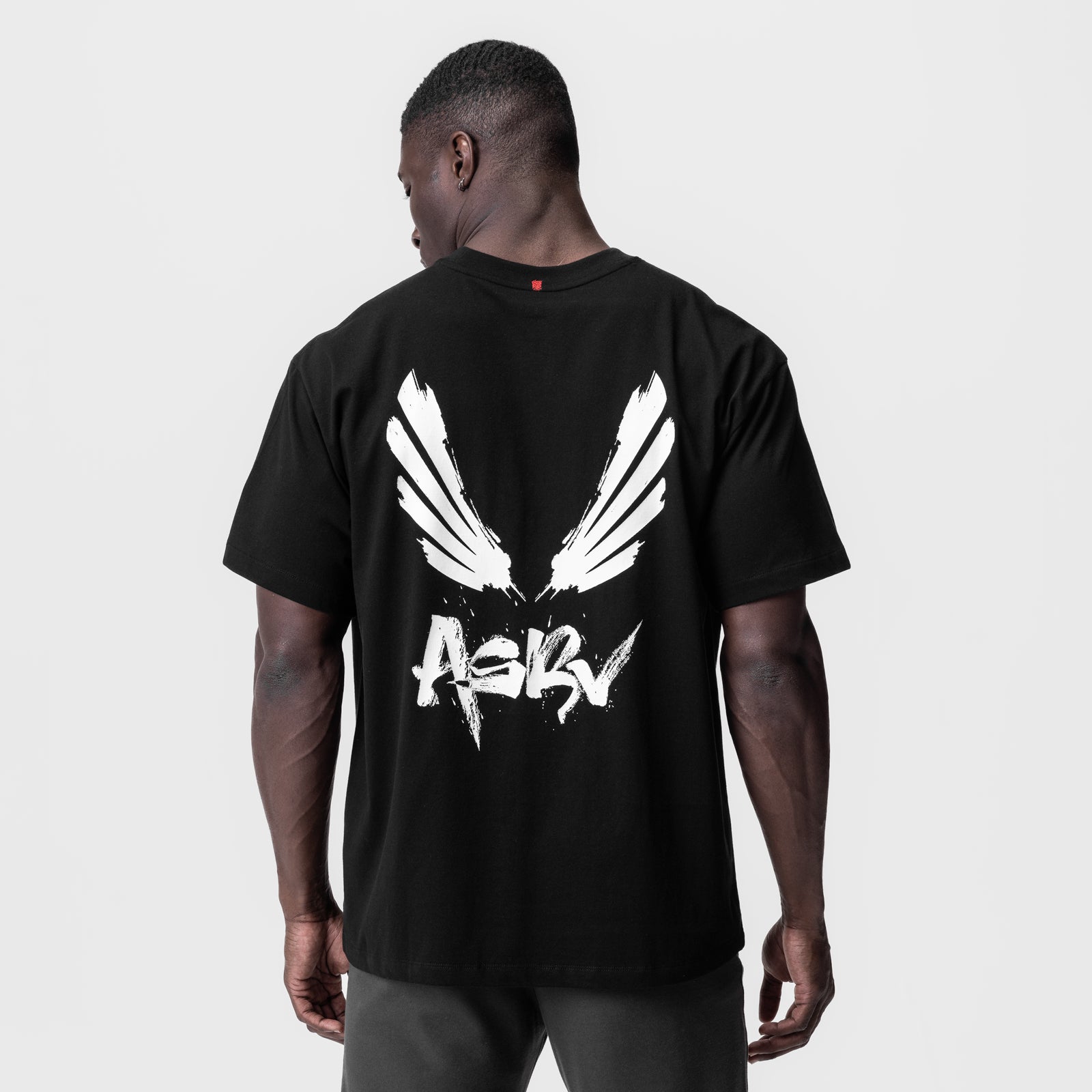 Black Tech Essential Relaxed Tee with white brush wings and ASRV logo, back view on model