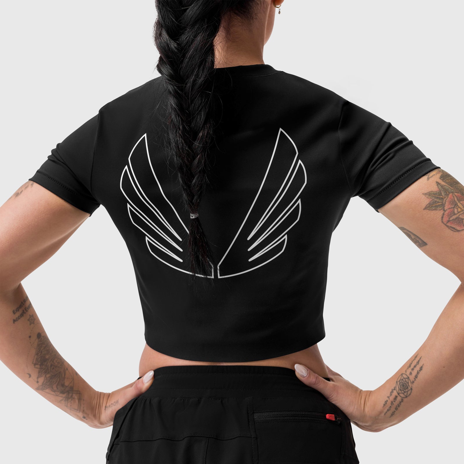 Black cropped tee with white wing graphic on back, worn by model with hands on hips