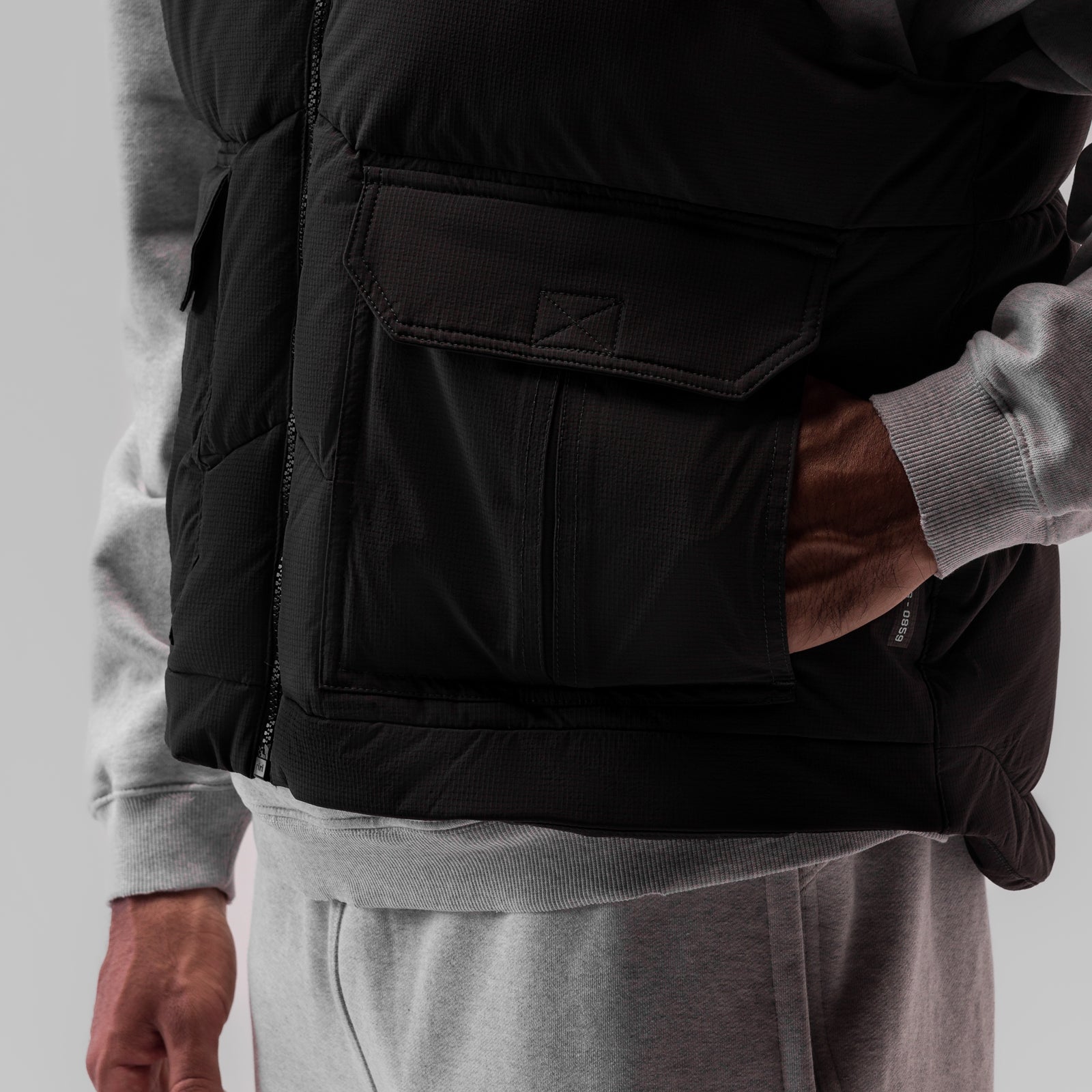 Black ripstop insulated puffer gilet worn over grey hoodie, side detail view
