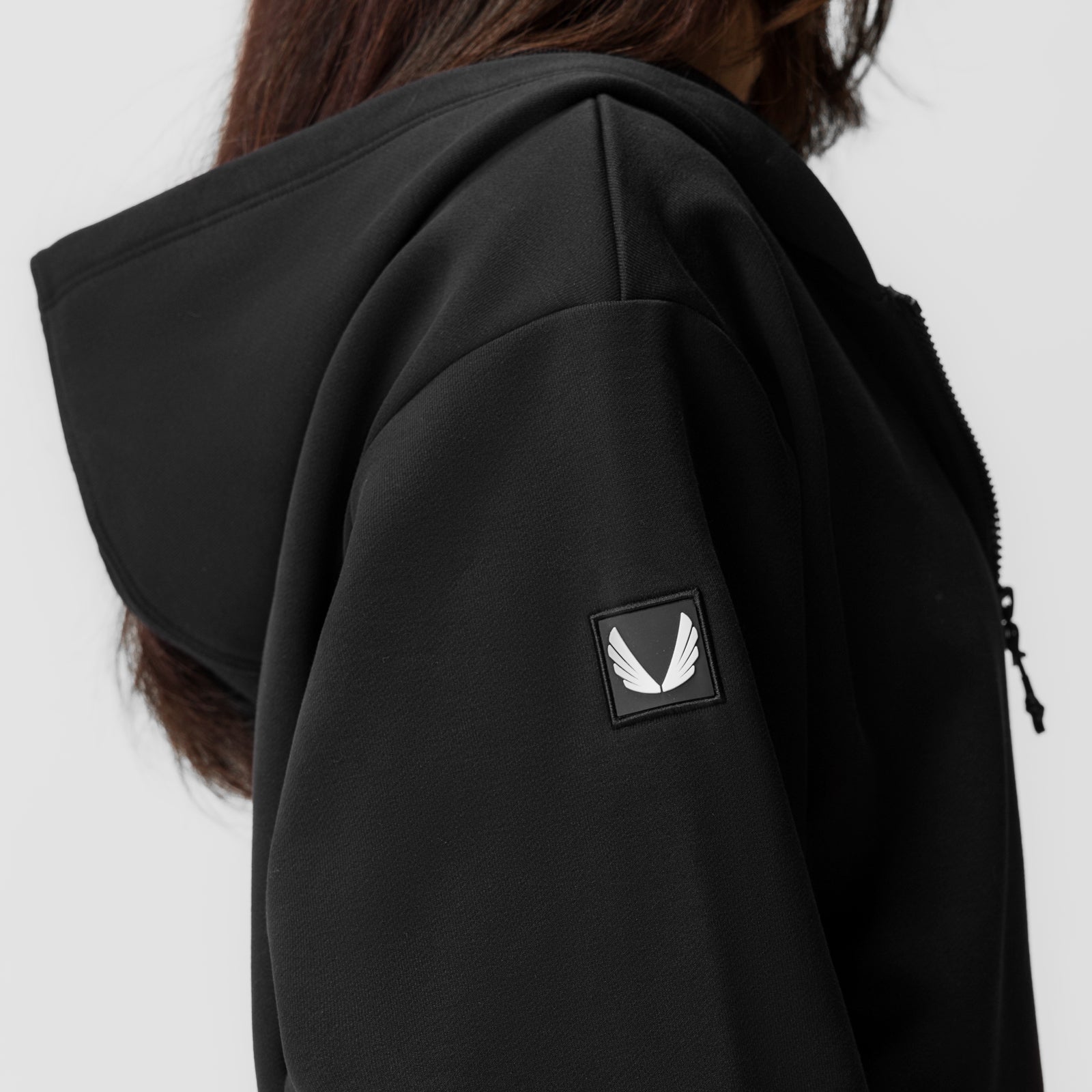 Black oversized zip hoodie worn by model, back view showing logo patch on sleeve