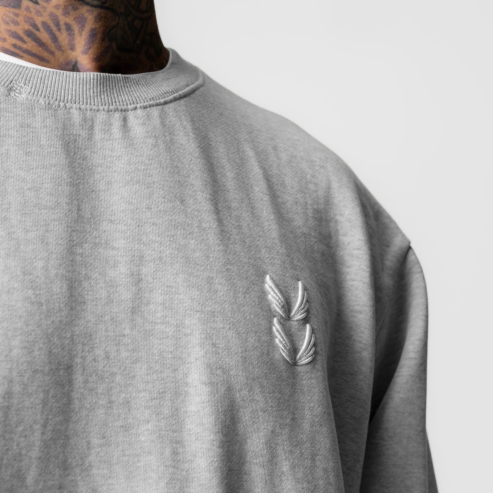Tech Essential Distressed Crewneck in heather grey, worn by model showing chest embroidery detail