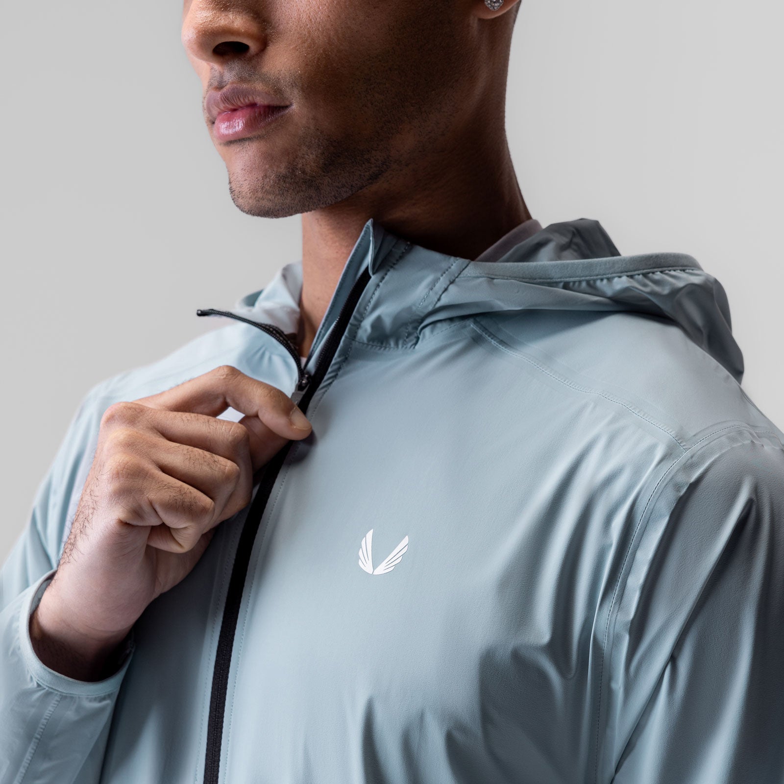 Aerotex Lightweight Windbreaker in light sky, worn by model holding hood drawstring