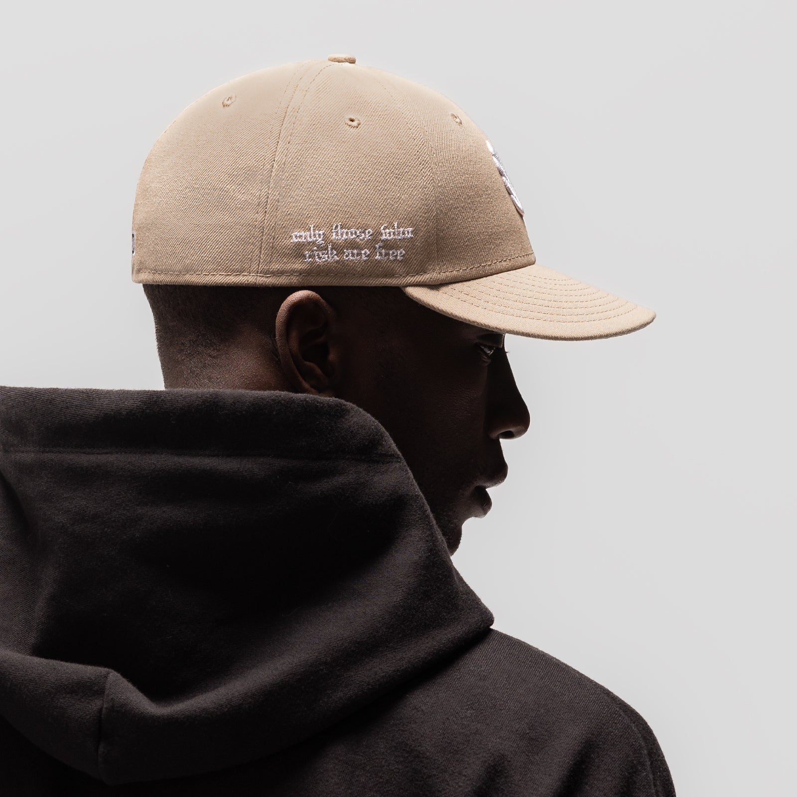 New Era 59Fifty Low Profile Hat in beige with white text, worn by model in profile view