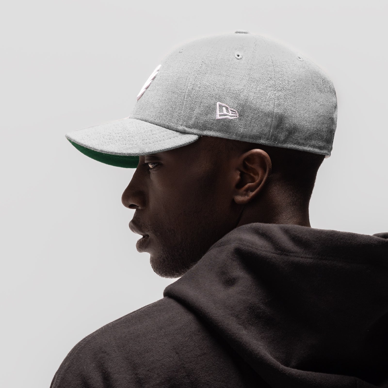 New Era 59Fifty Low Profile Hat in heather grey with white and green accents, worn by model in profile