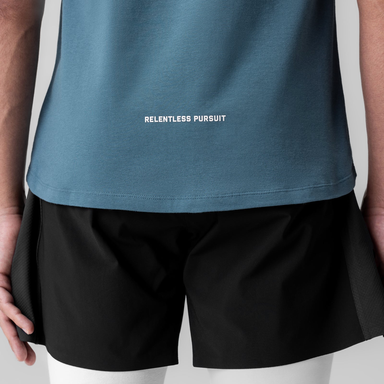 Creora® Cotton Modal Cutoff Tank in storm blue worn by model with black shorts, showing 'Relentless Pursuit' text