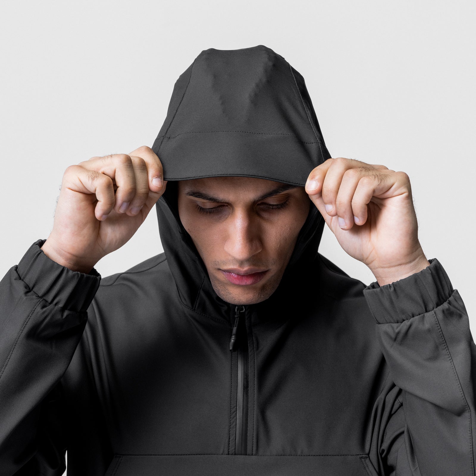 Black weather-ready anorak jacket worn by model pulling hood down, front view