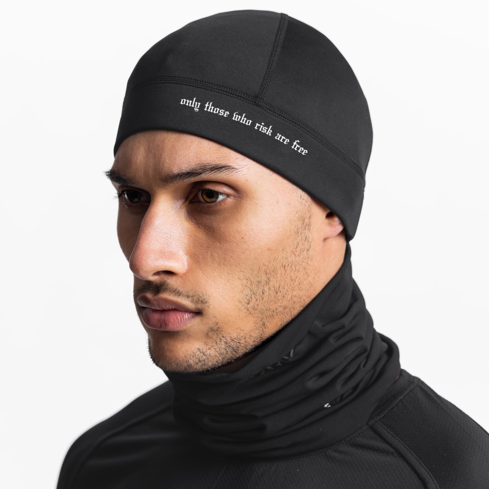 Black performance skull cap with "only those who risk are free" text, worn by model in profile