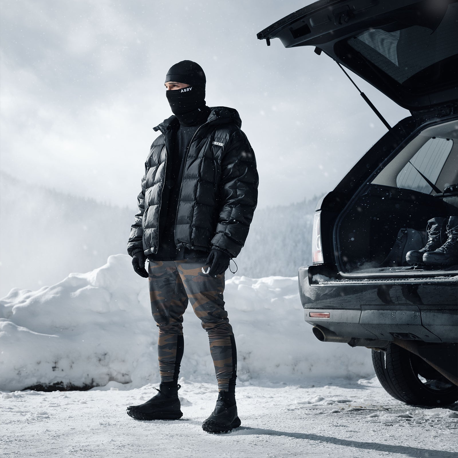 Weather-Ready Down Puffer Jacket in black, worn by model standing next to open car in snowy mountain setting