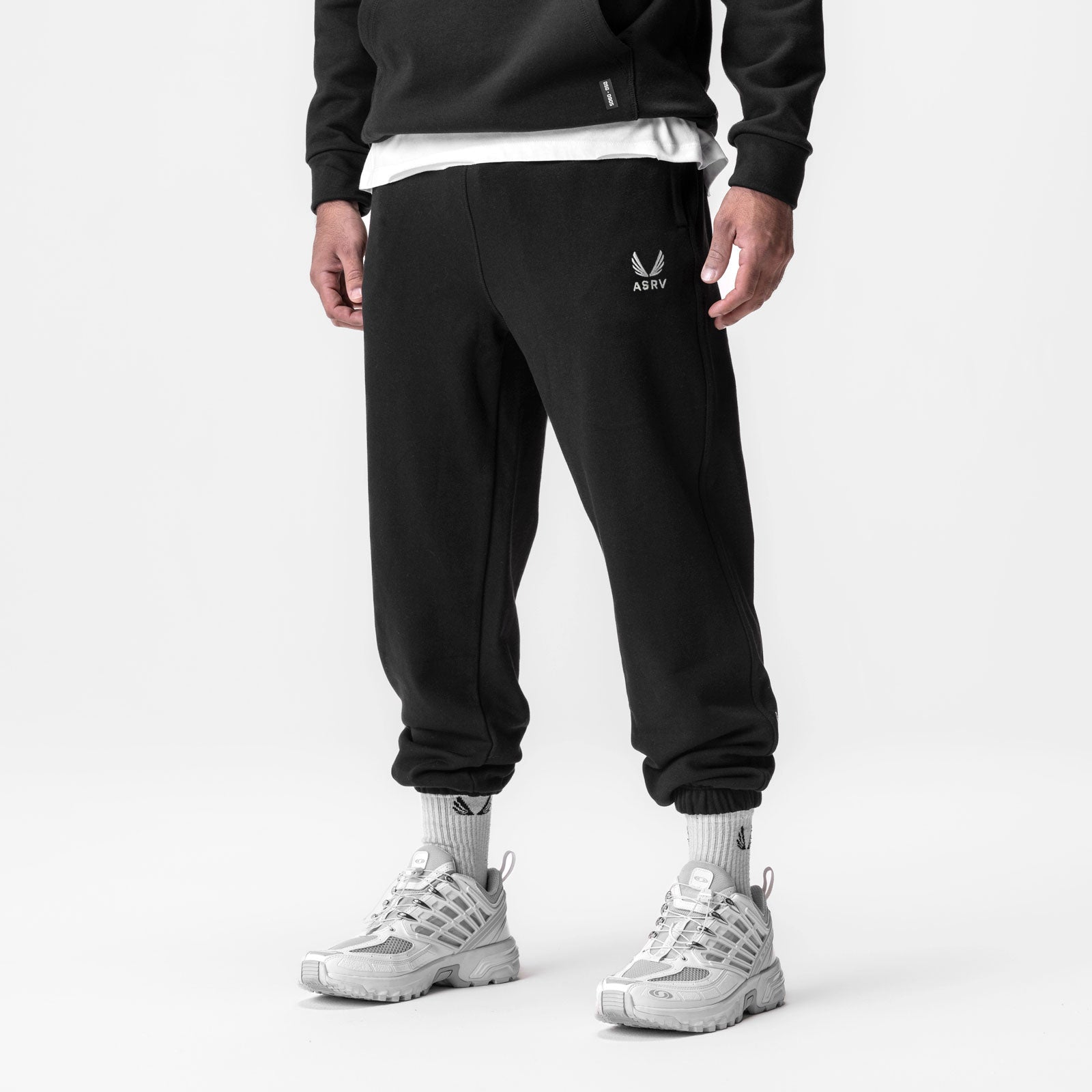 Black Tech-Terry oversized sweatpants with ASRV emblem, worn with white sneakers and socks, front view