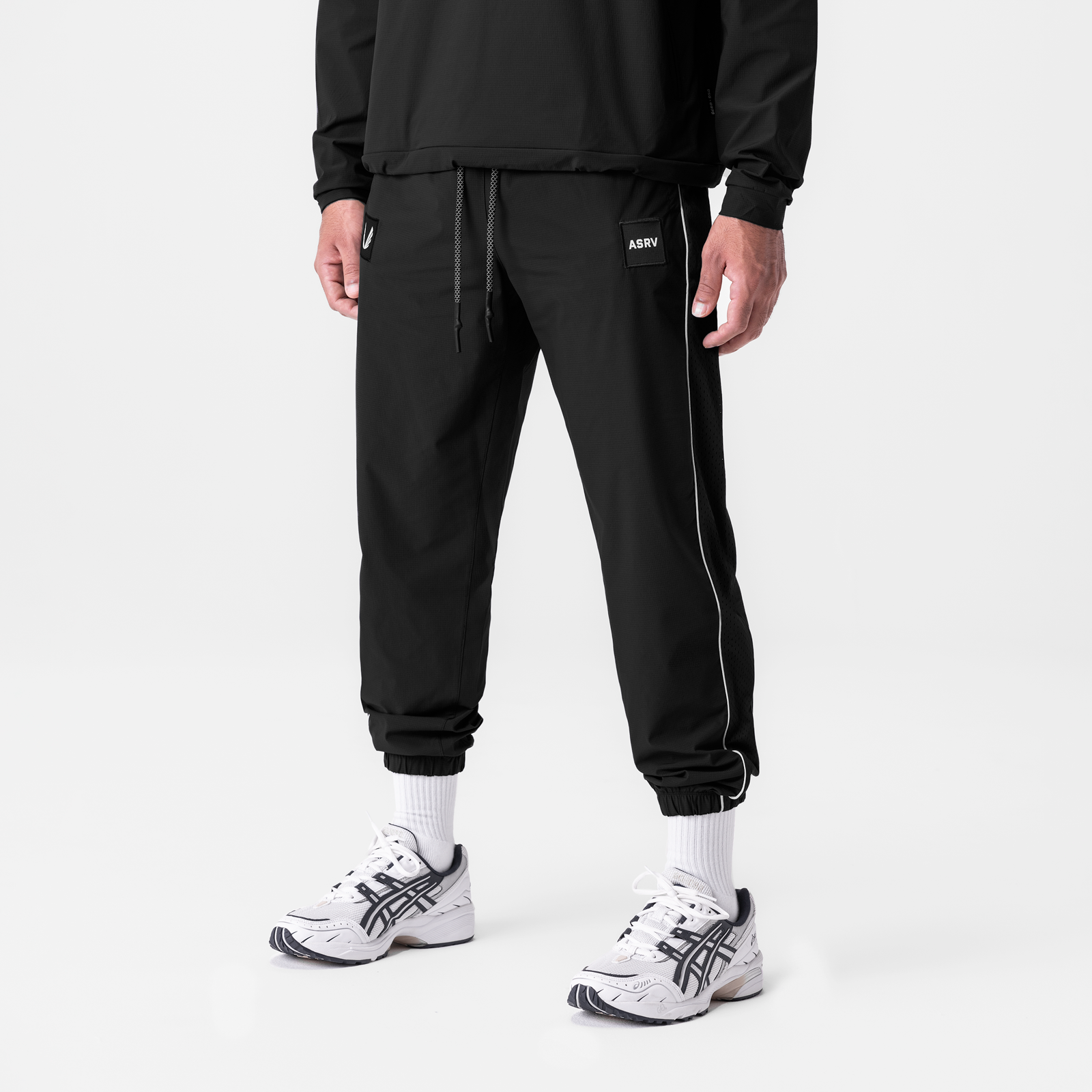 Black ripstop oversized track pants with side stripe worn with white socks and sneakers, front view