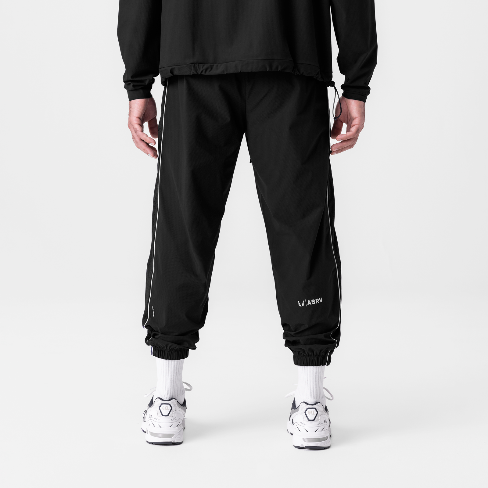 Black ripstop oversized track pants with side stripe, back view on model wearing white socks and sneakers