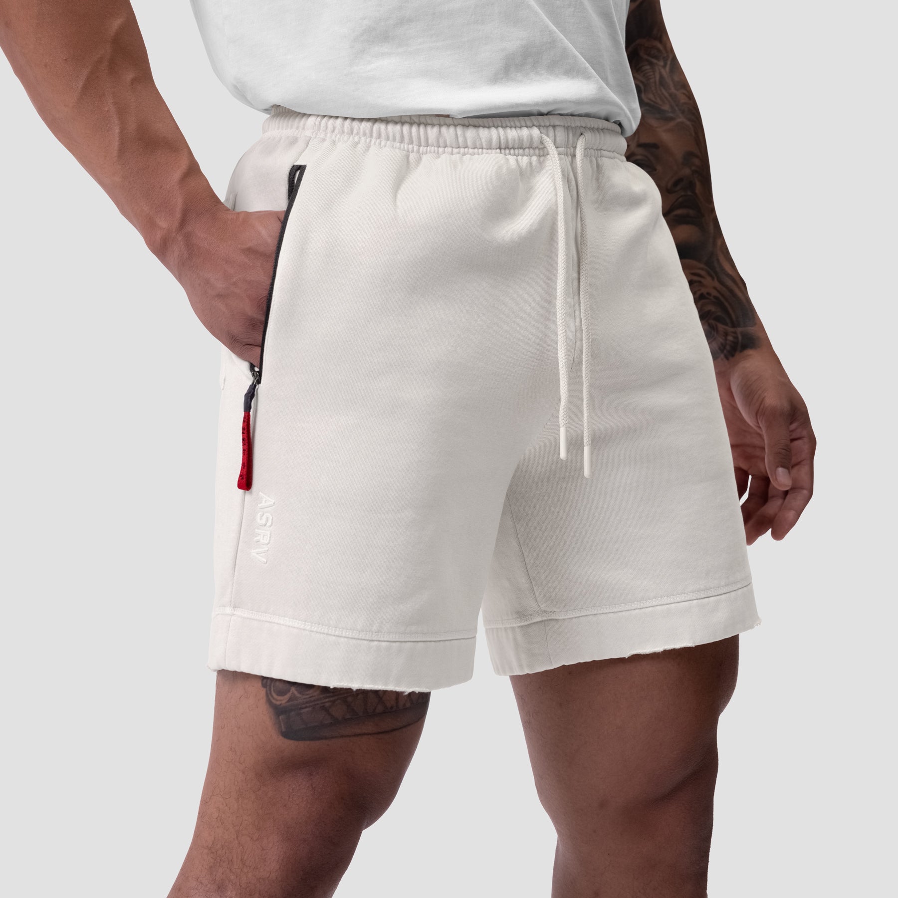 Tech Essential Sweat Short in cream worn by model, side view with hands in pockets