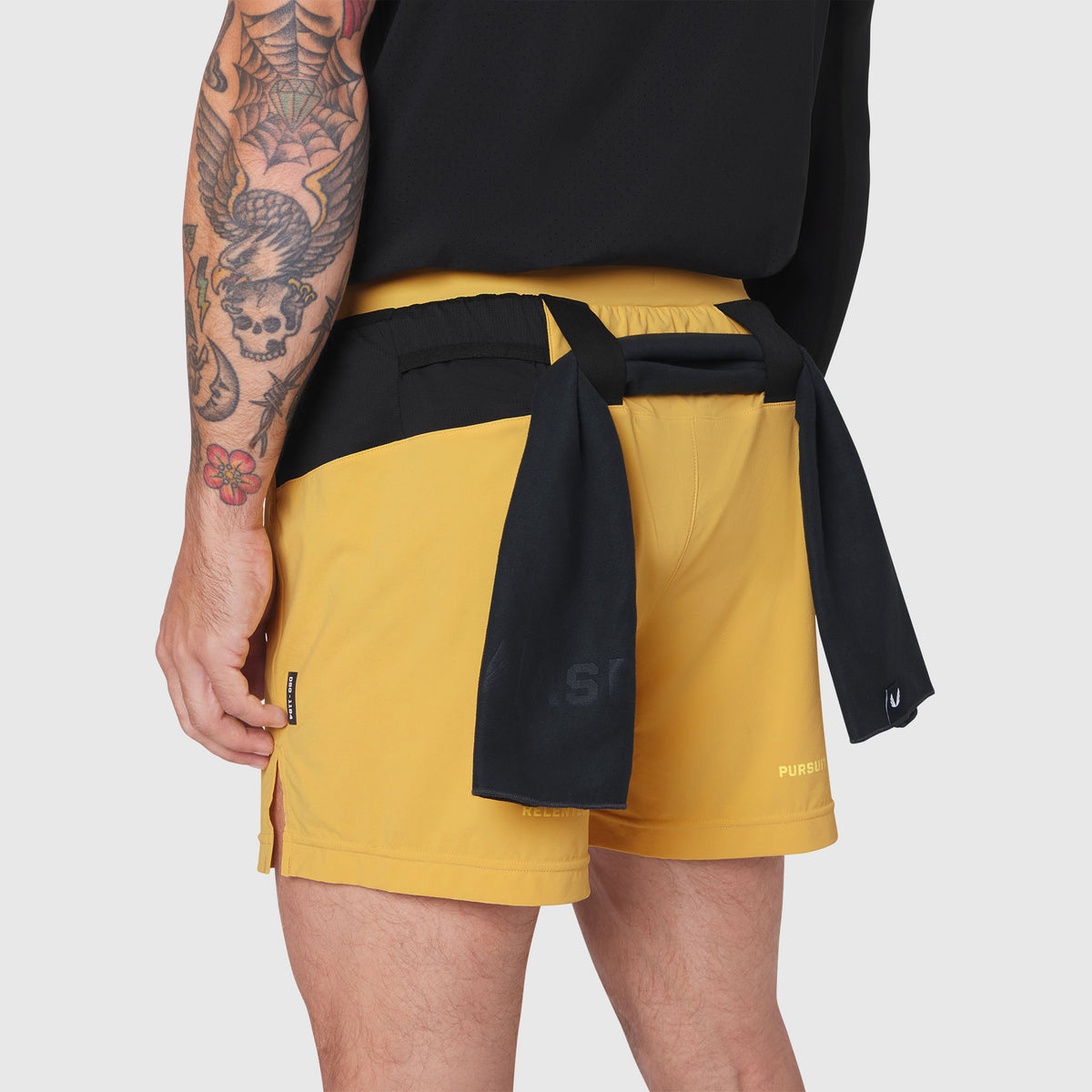 Aerotex Distance Run Short in amber yellow worn by model, back view with black shirt tied at waist