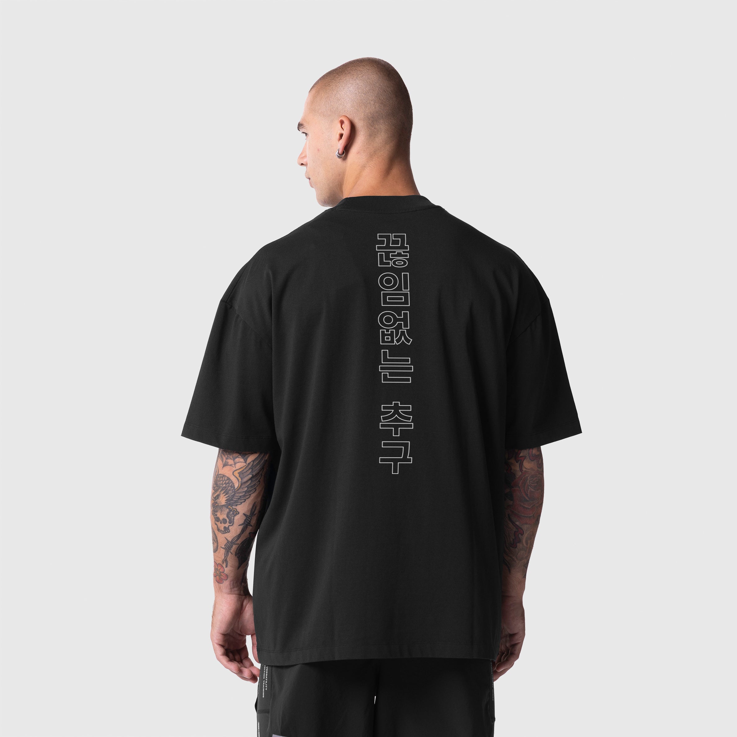 Model wearing black ASRV Tech Essential Oversized Boxy Tee with Korean characters on back, shown from rear view.