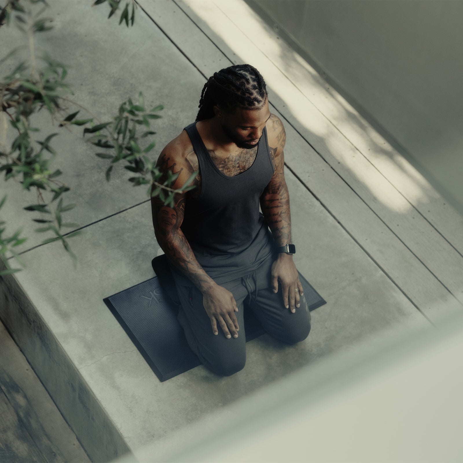 Man wearing black ASRV meditation bench outfit, kneeling on mat in minimalist space
