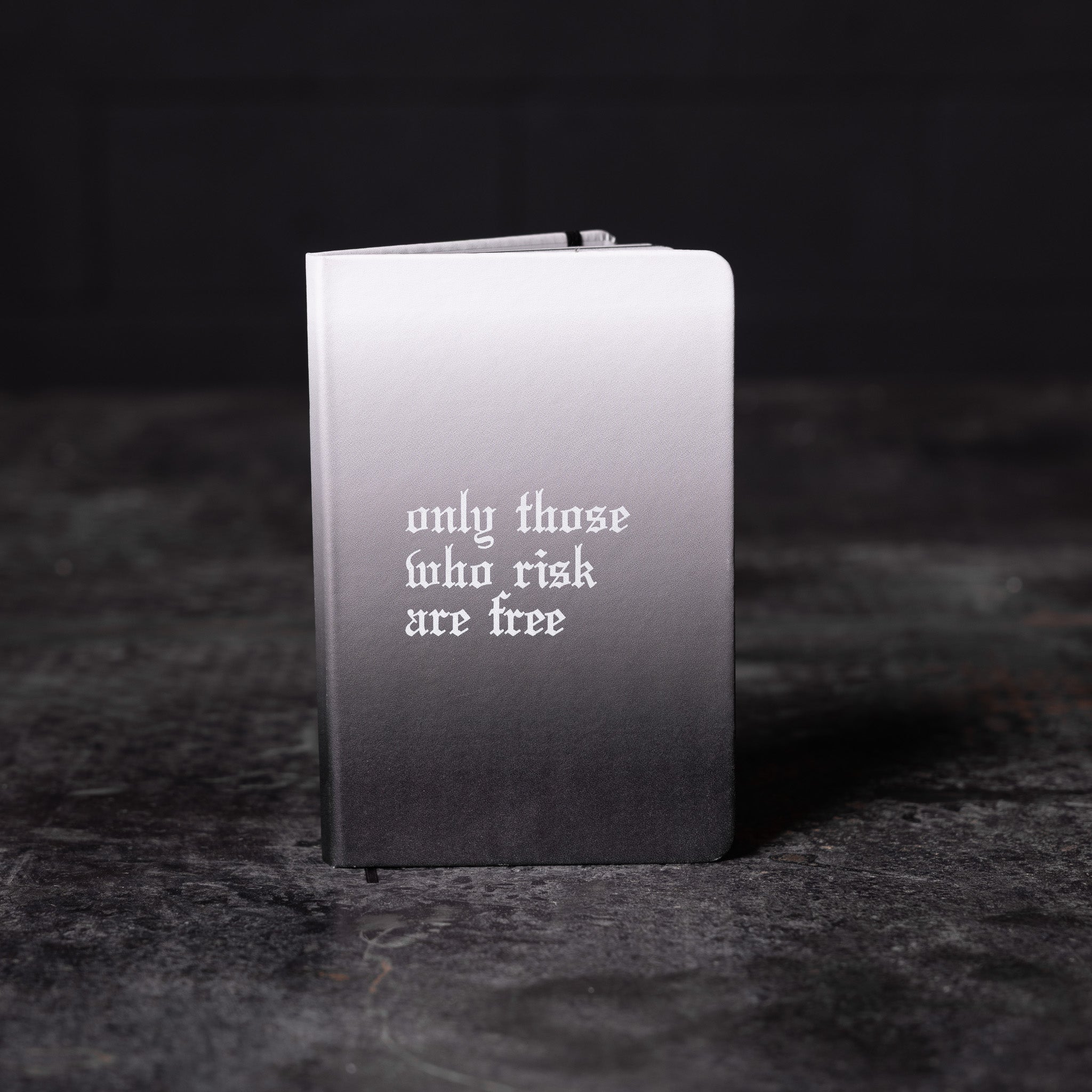 flatlay SM'22 OTWR Notebook in black and white gradient, front view on dark surface