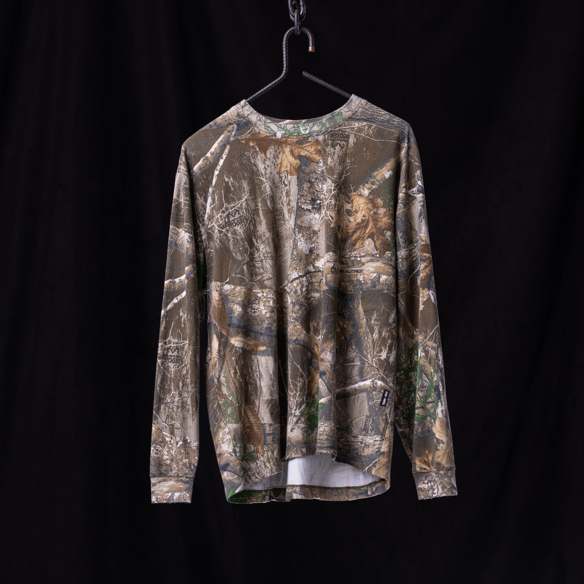 FA'23 Relaxed Long Sleeve in realtree camo, hung on black hanger against dark background