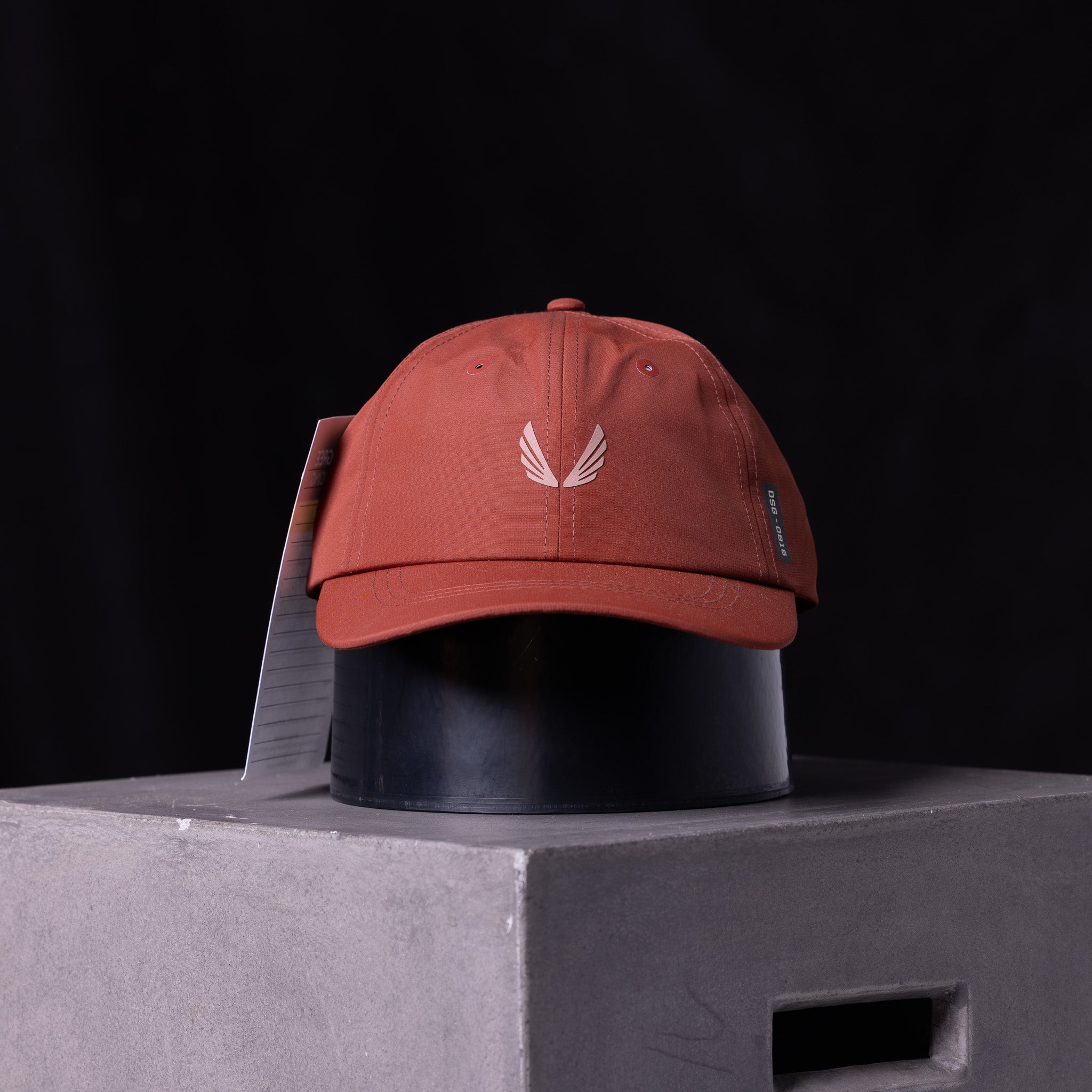 flatlay SP'23 Hybrid Sport Cap in rust red with white wing logo, front view