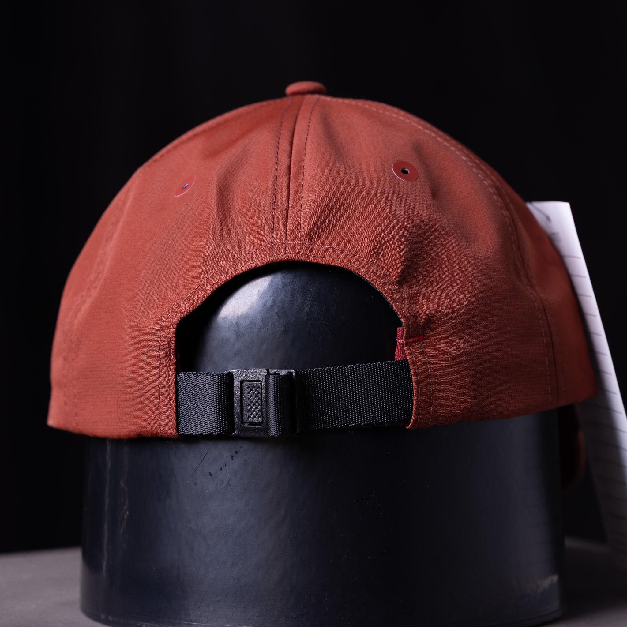 SP'23 Hybrid Sport Cap in rust red with black strap, displayed on mannequin head against dark background