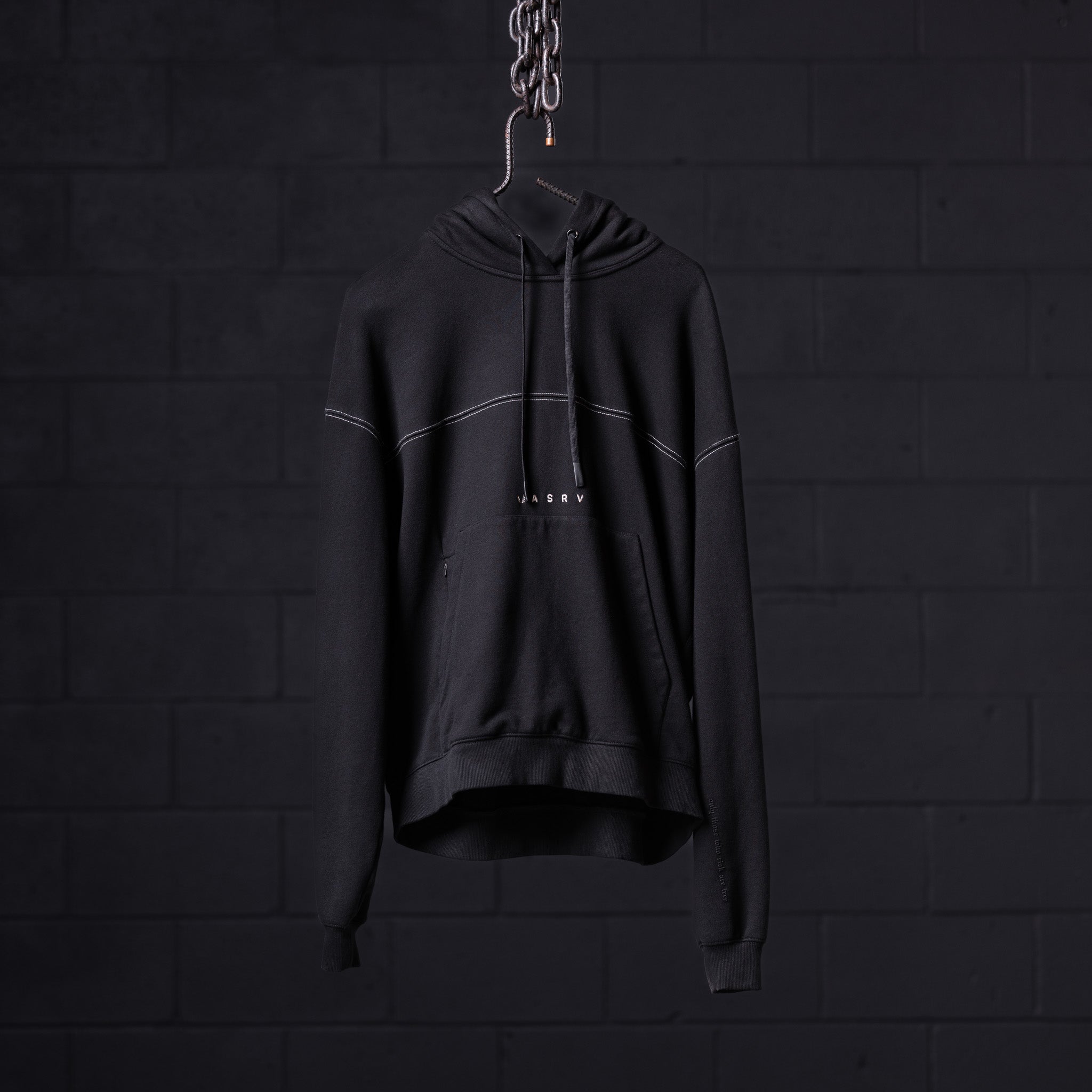Black contrast thread hoodie displayed on hanger against dark brick wall