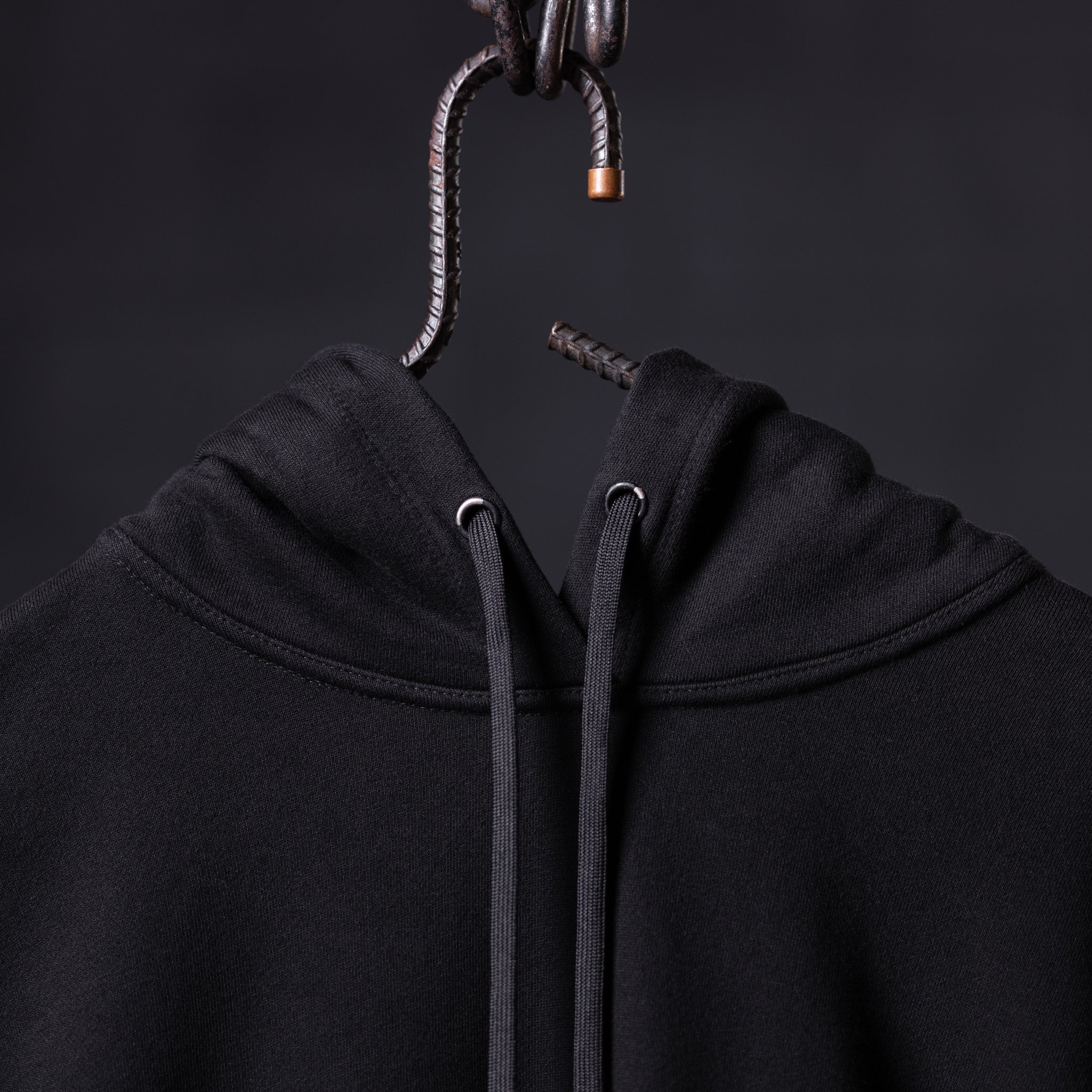 FA'20 Contrast Thread Hoodie in black, hung on metal hook showing drawstring detail