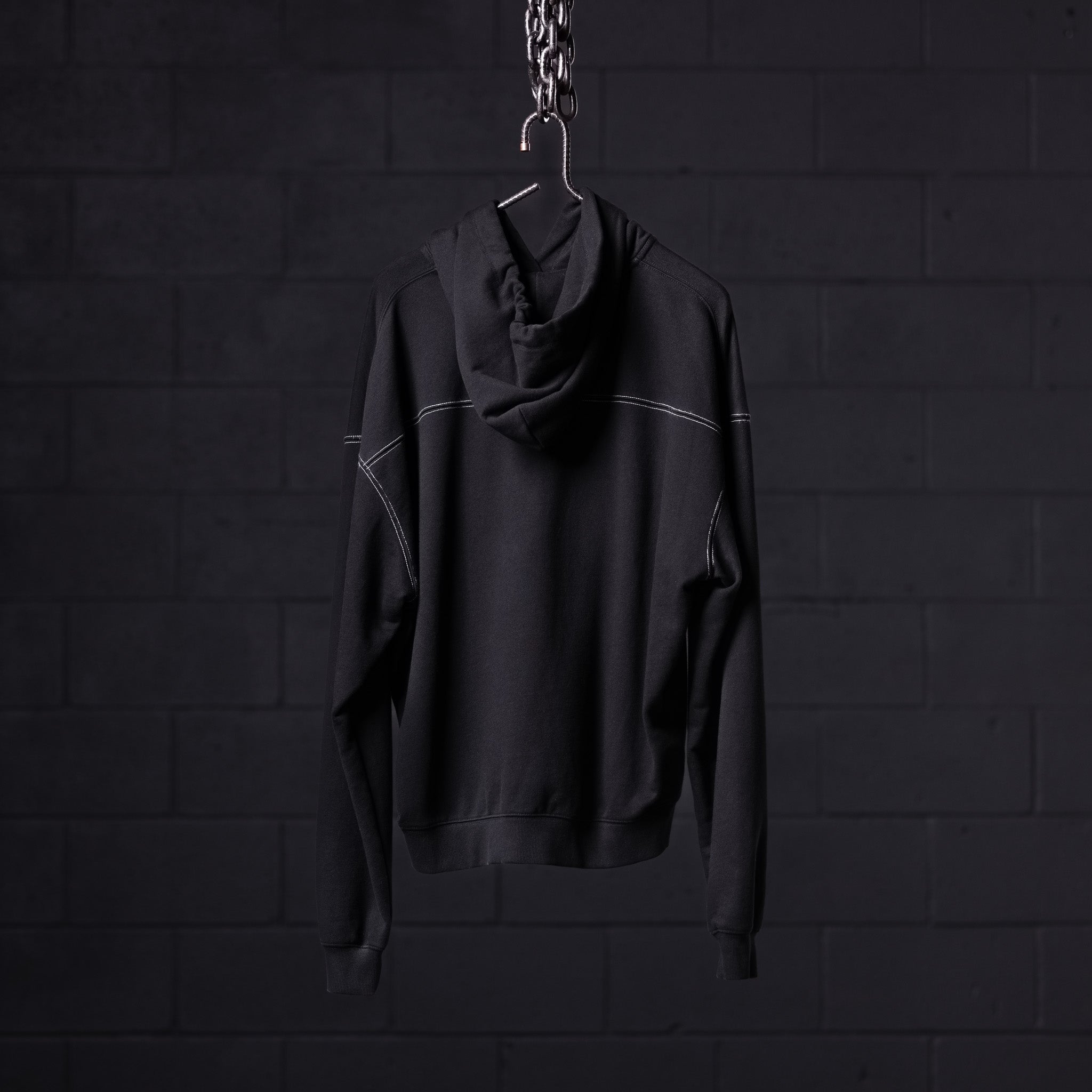 Black contrast thread hoodie displayed on hanger against dark brick wall background