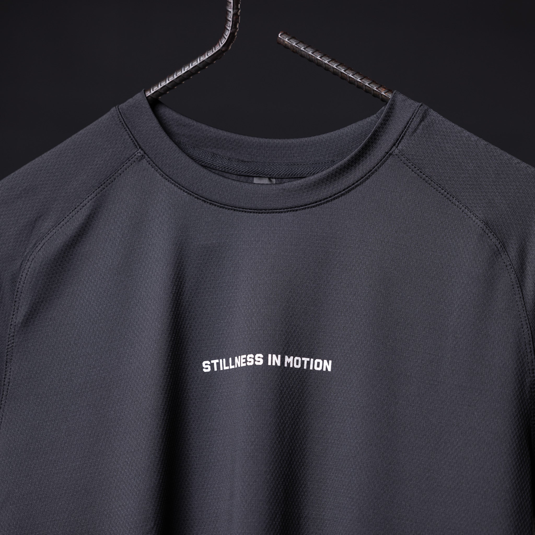 SM'22 Established Tee in charcoal gray on hanger, front view showing 'Stillness in Motion' text