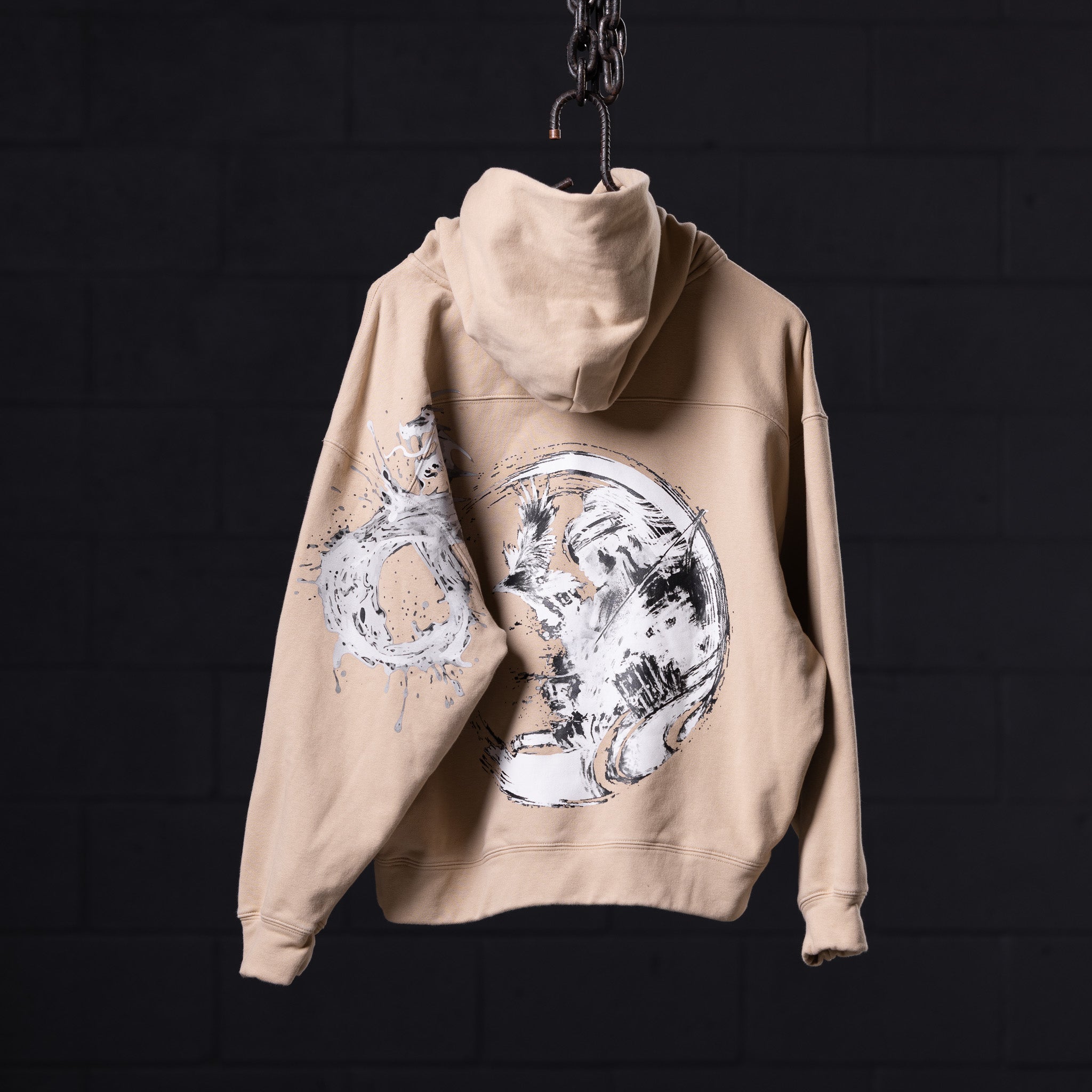 Beige graphic hoodie with white celestial moon designs, hung on chain against dark background