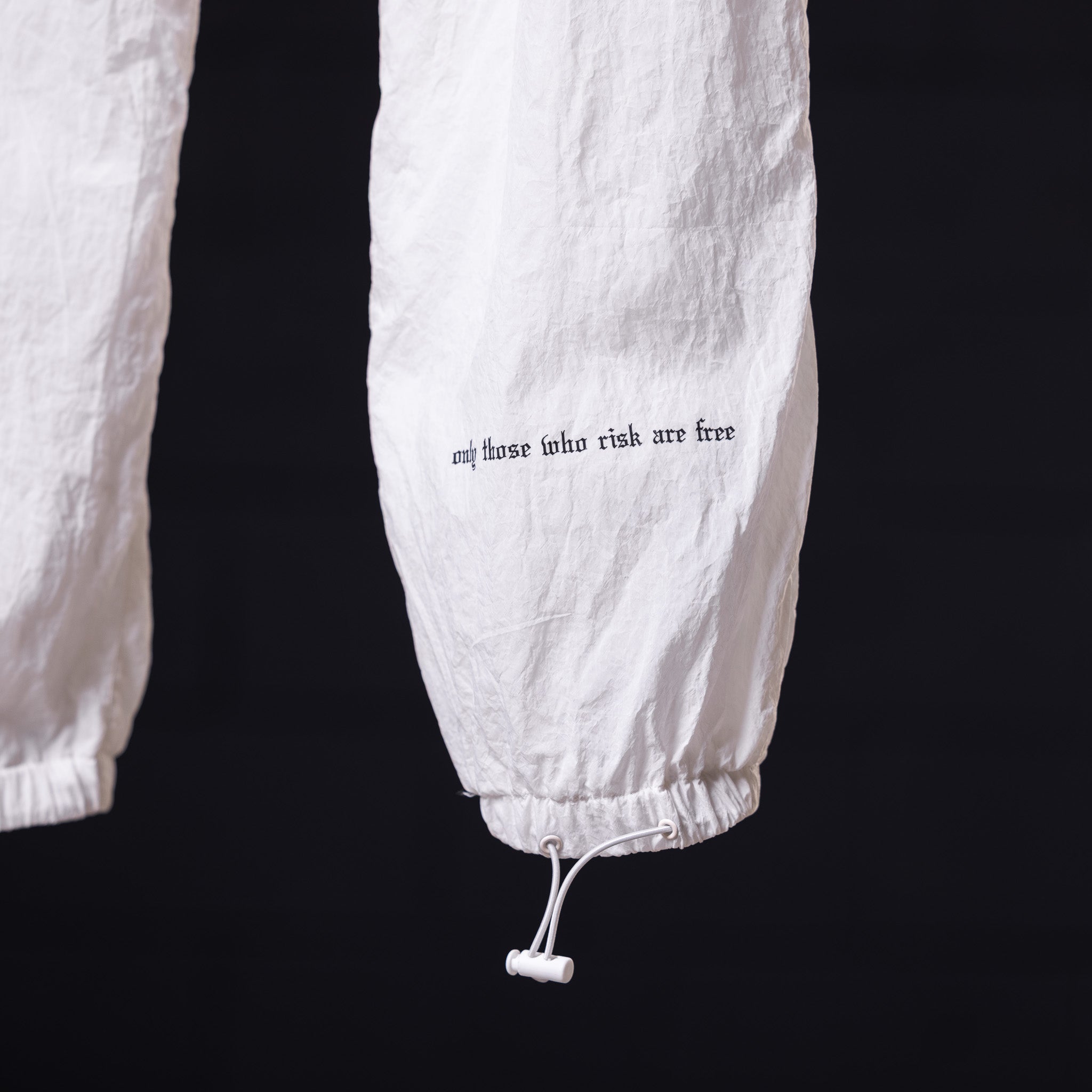 Oversized track pant in white with text detail on leg, close-up view