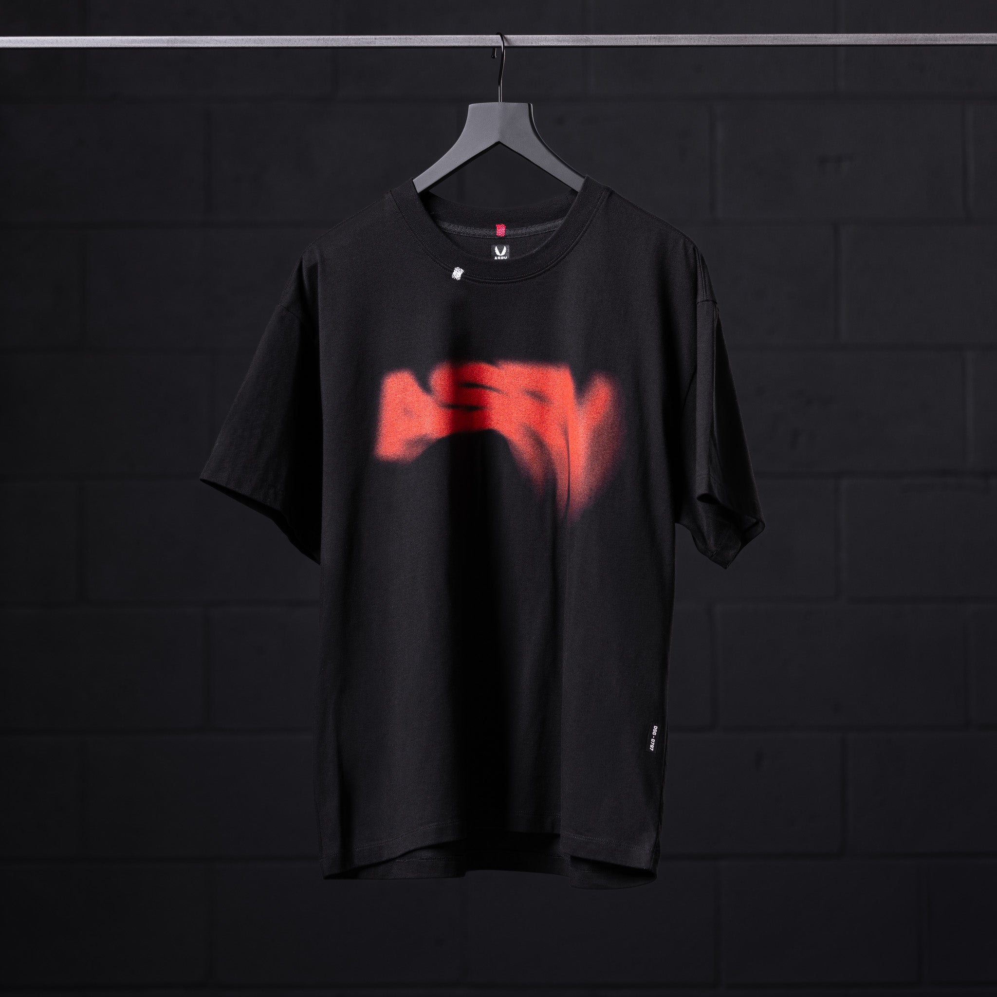Black Tech Essential Relaxed Tee with red graphic print on hanger against dark background