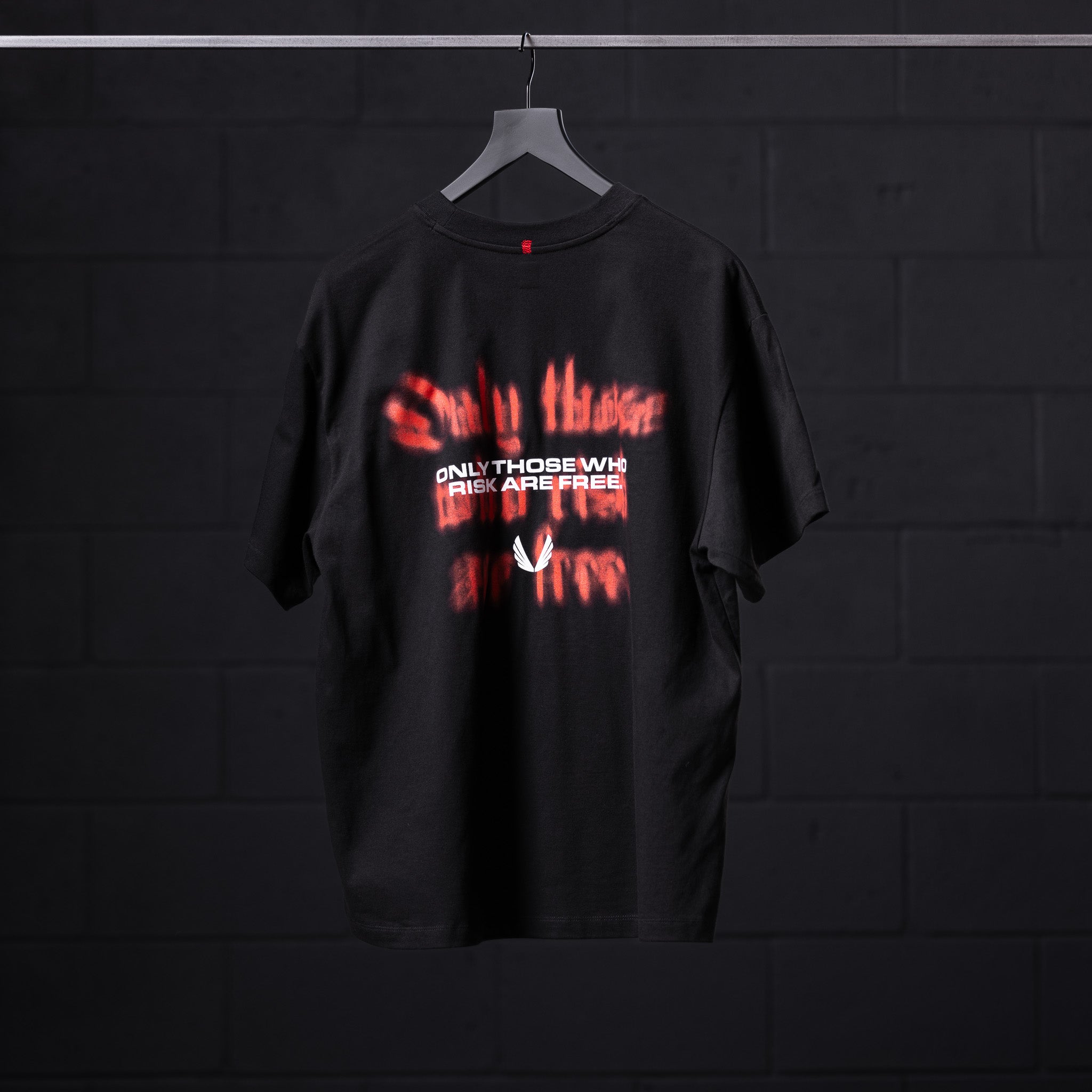 Black Tech Essential Relaxed Tee with red 'Risk Protocol' graphic design, displayed on hanger