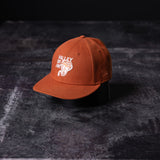 flatlay SM'23 Valley of Fire Low Pro Hat in rust orange, front view on dark textured surface